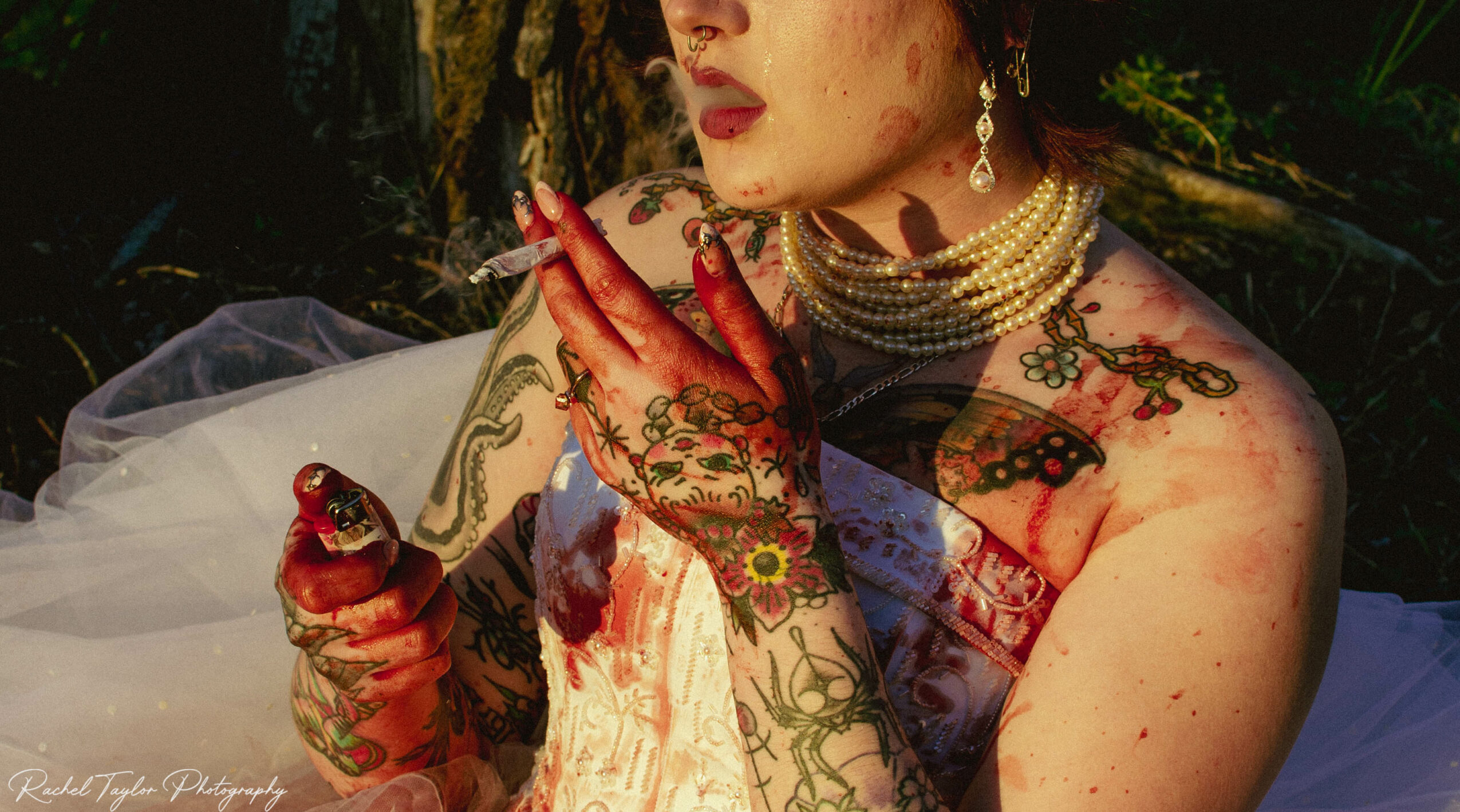 Person with henna tattoos, jewelry, and makeup, holding a blood-stained cloth, outdoors with greenery in background.