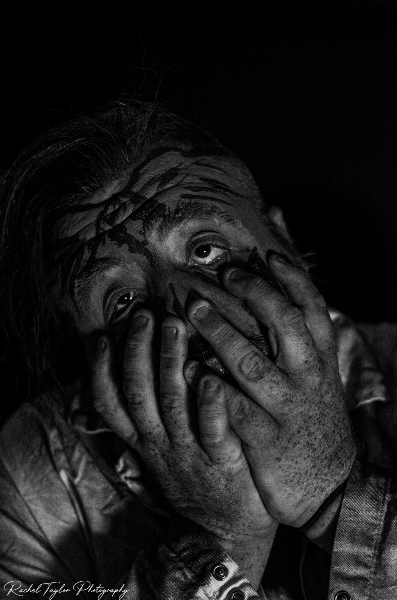 Person with hands covering face, eyes wide open, in black and white, showing distress or fear.