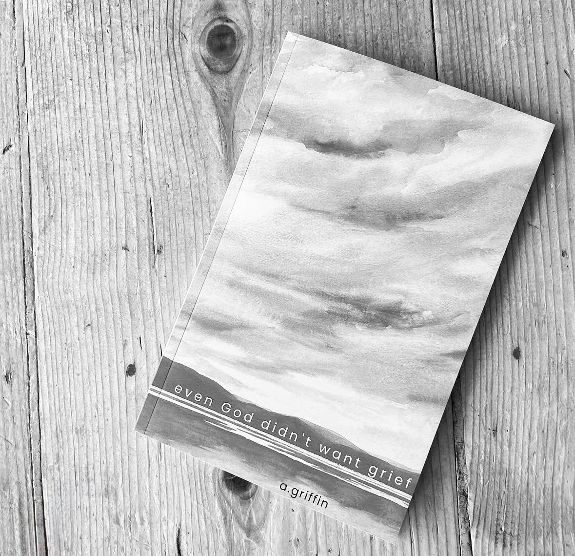 Book with cloudy sky cover on wooden surface, title reads 'even god didn't want glory', author 'a.griffin'.