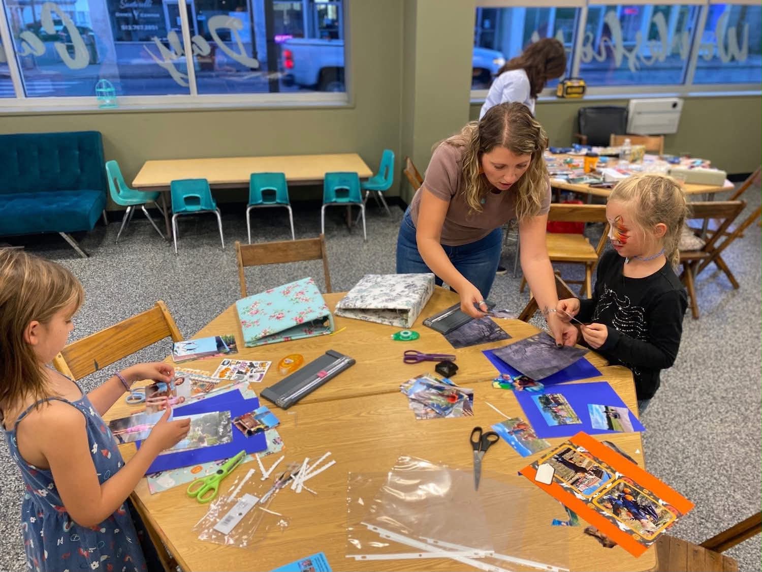 Children and an adult working on arts and crafts at a table in a classroom, with supplies scattered around.