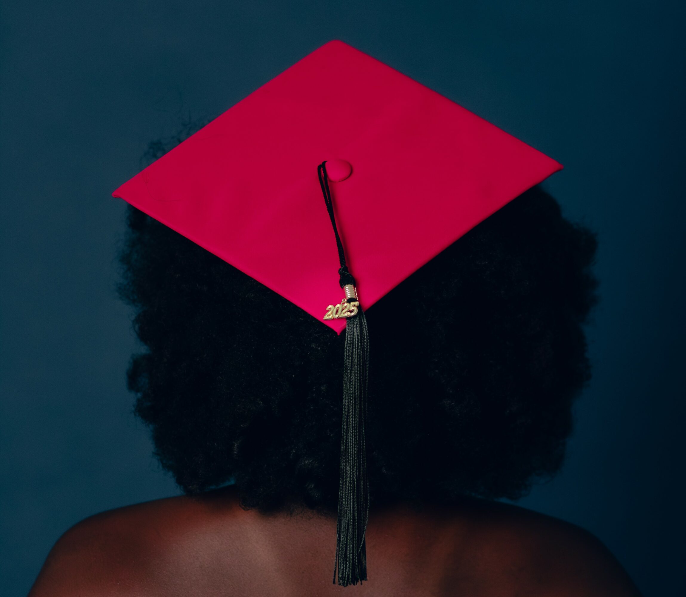 Person with curly hair wearing a red graduation cap with a black tassel, viewed from behind.