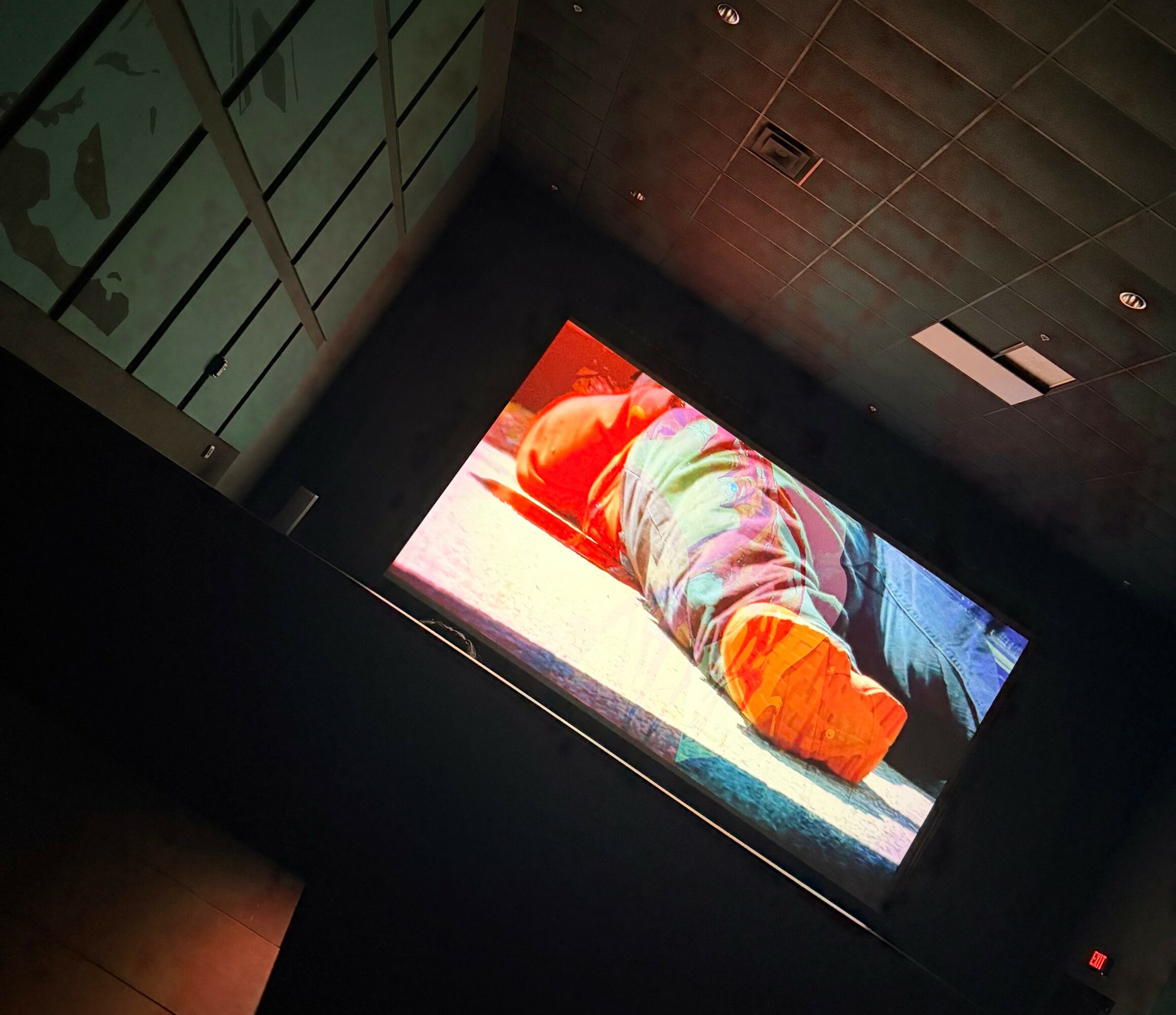 Large screen displaying a person lying down, with a colorful background, in a dark room with a high ceiling.