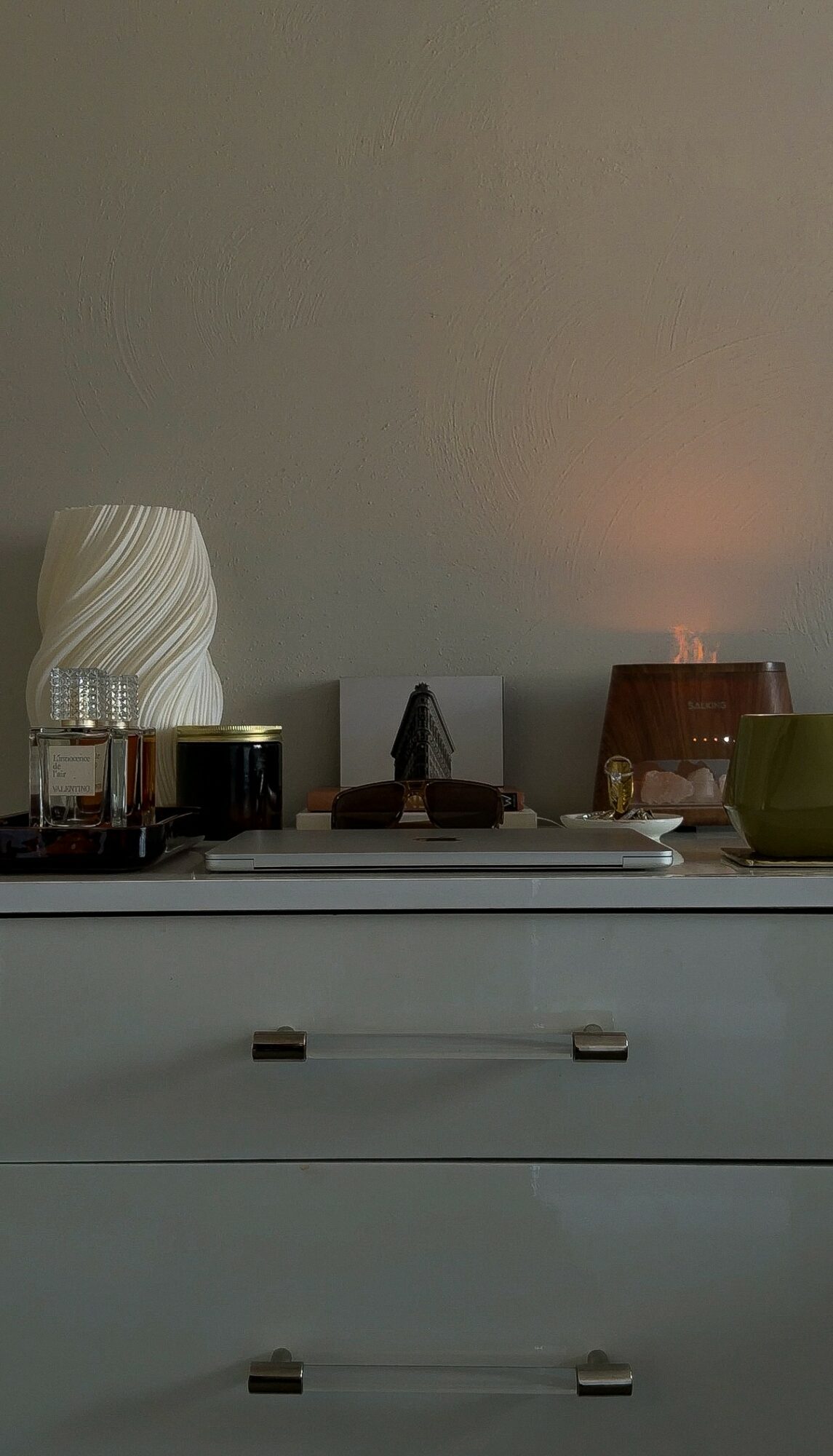 Shelf with decorative objects, including a white vase, candles, and a small sculpture, against a plain wall.