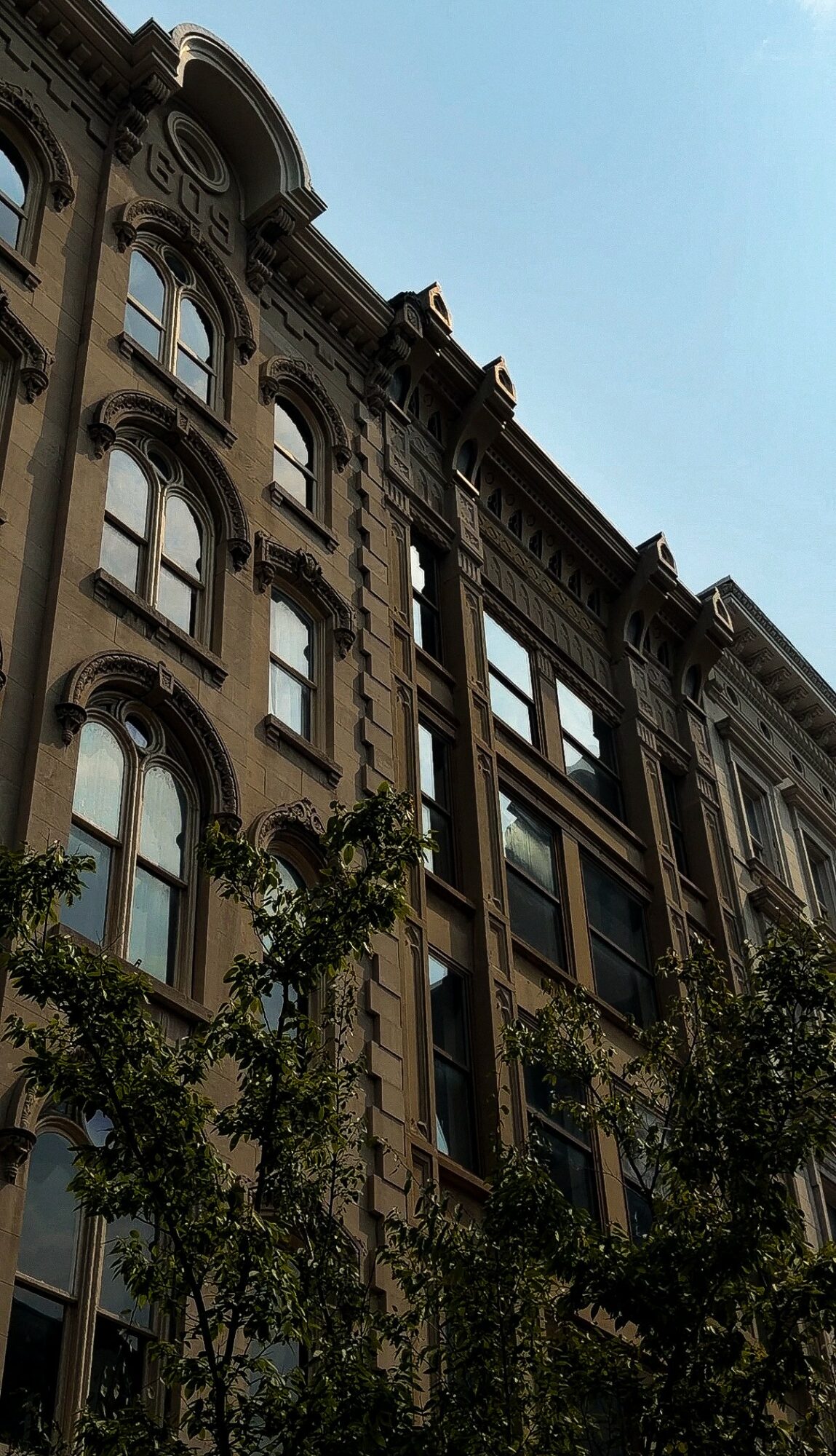 Upright view of a historic multi-story building with ornate architectural details and large windows, against a clear blue sky.