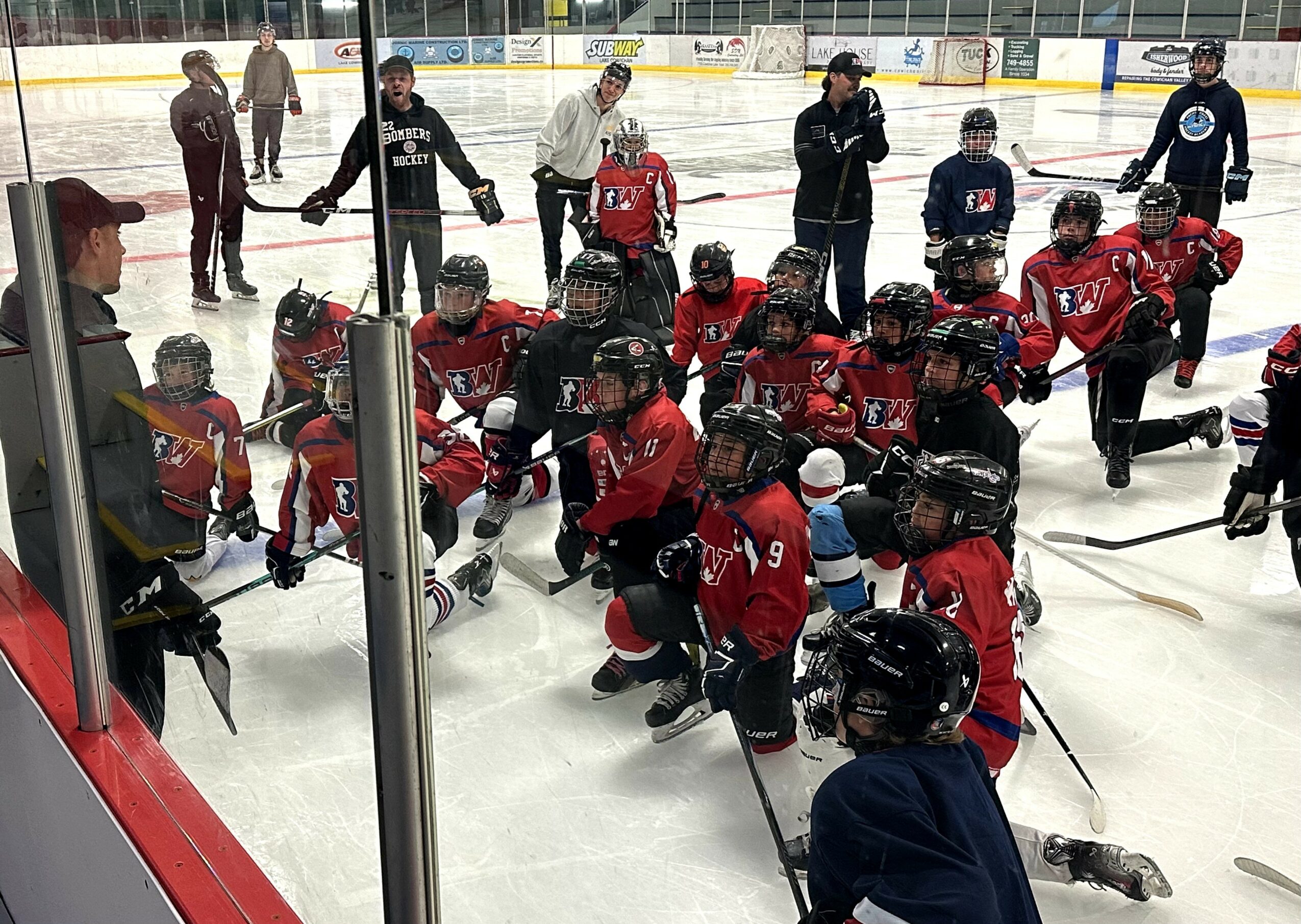 Hockey team in red jerseys kneeling and standing on ice rink, players and coach gathered after game or practice.