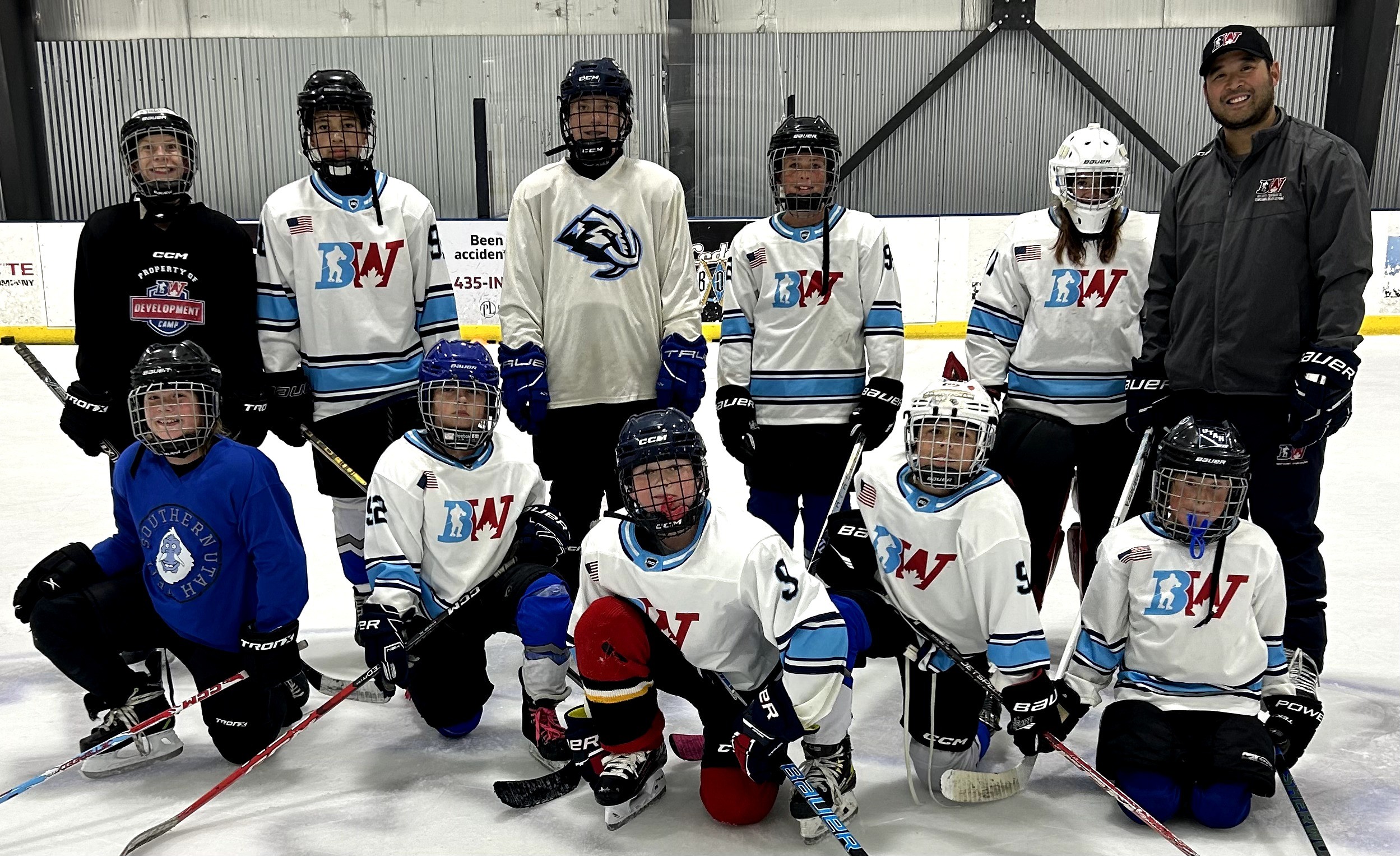 Group of young hockey players and coach on ice rink, wearing jerseys and helmets, posing for a team photo.
