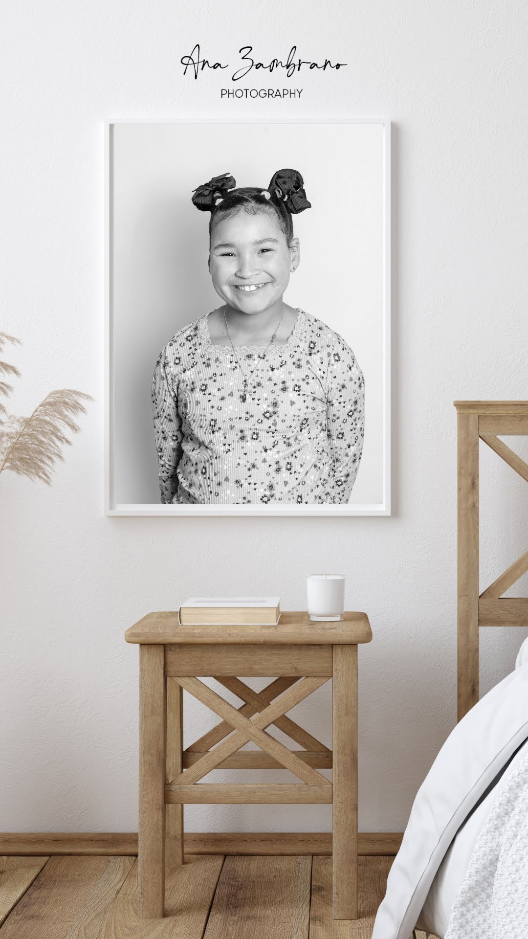 Black and white portrait of a smiling girl with two buns, hanging on a white wall above a wooden table.