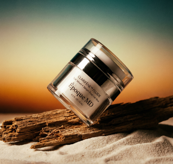 A jar of skincare cream tilted on a piece of driftwood with a sunset background.