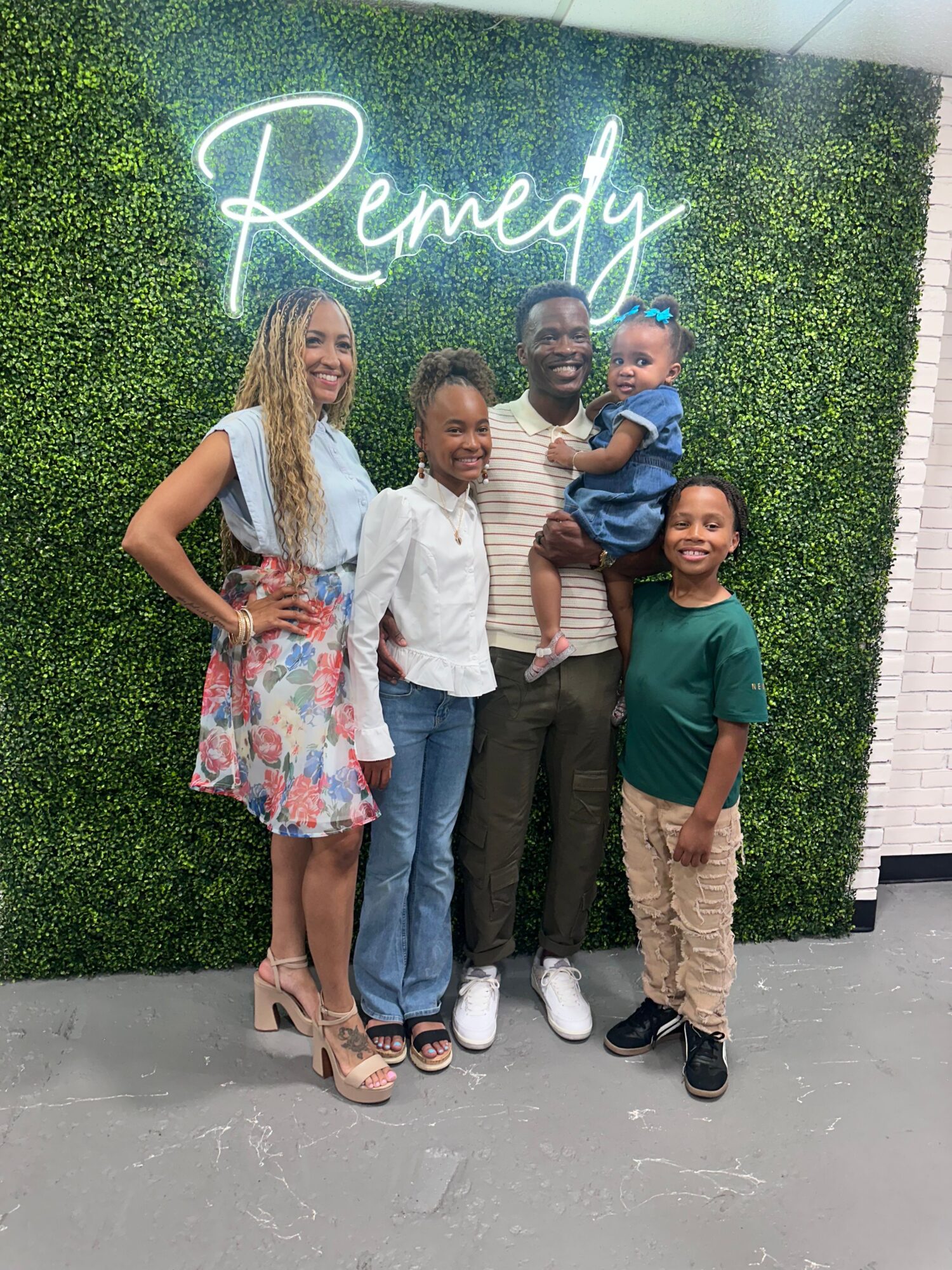 Four people pose in front of a green wall with a cursive sign.