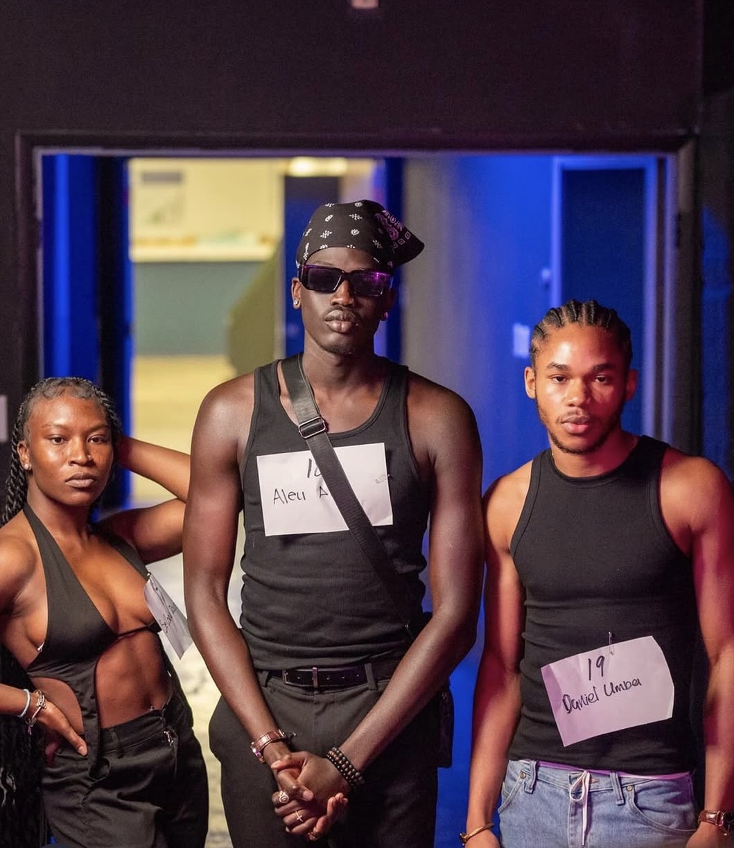 Three young people standing together indoors, wearing black tank tops and jeans, with name tags on their chests.