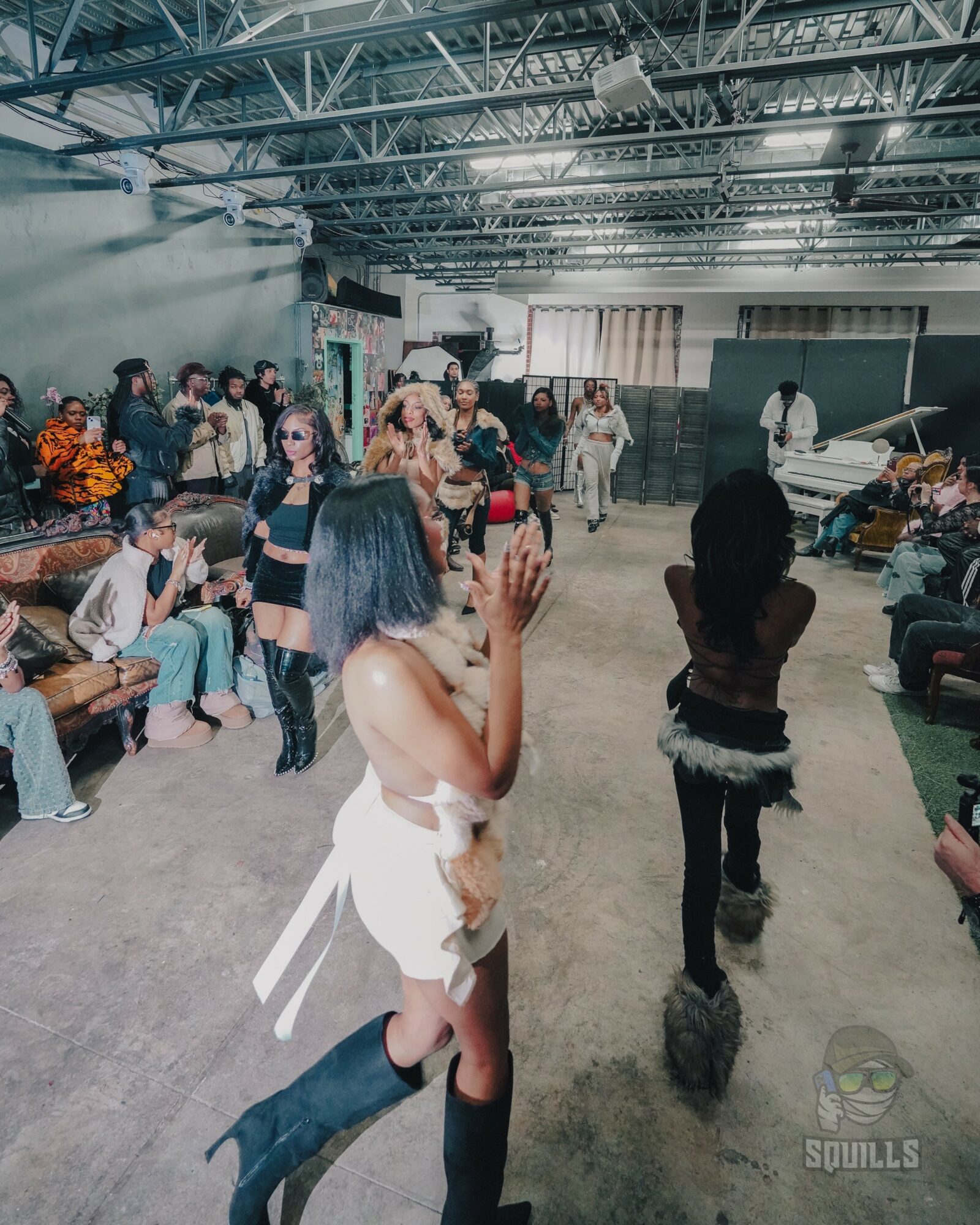 Group of people gathered indoors, some sitting and some standing, with a woman in the foreground raising her hand.