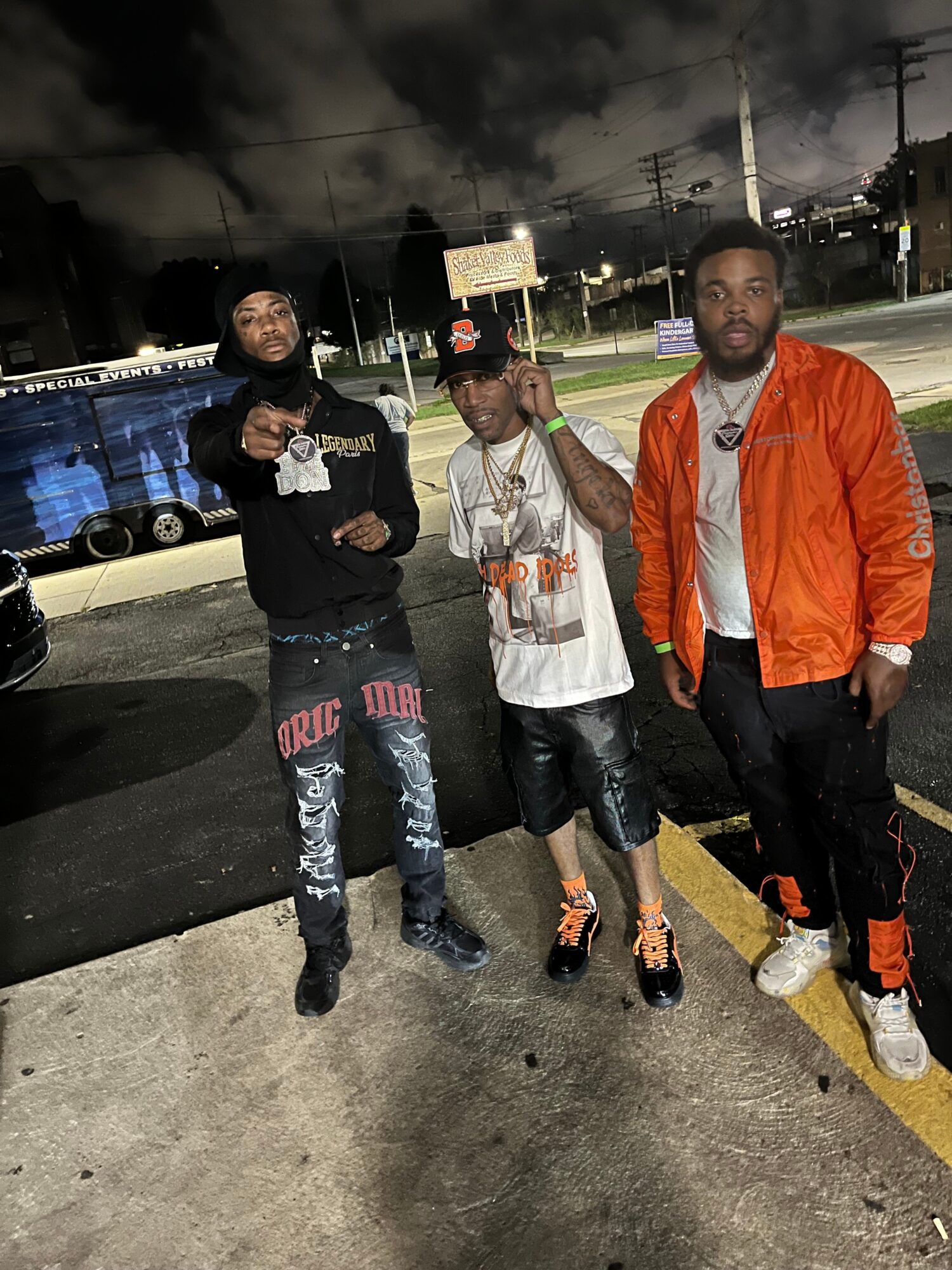 Three people stand beside a track at night, wearing casual clothing and sneakers.