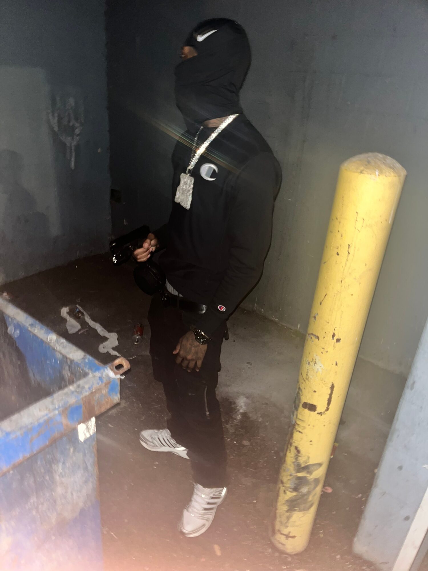 Two people in dark clothing stand beside a yellow pipe and blue equipment in a dim room.
