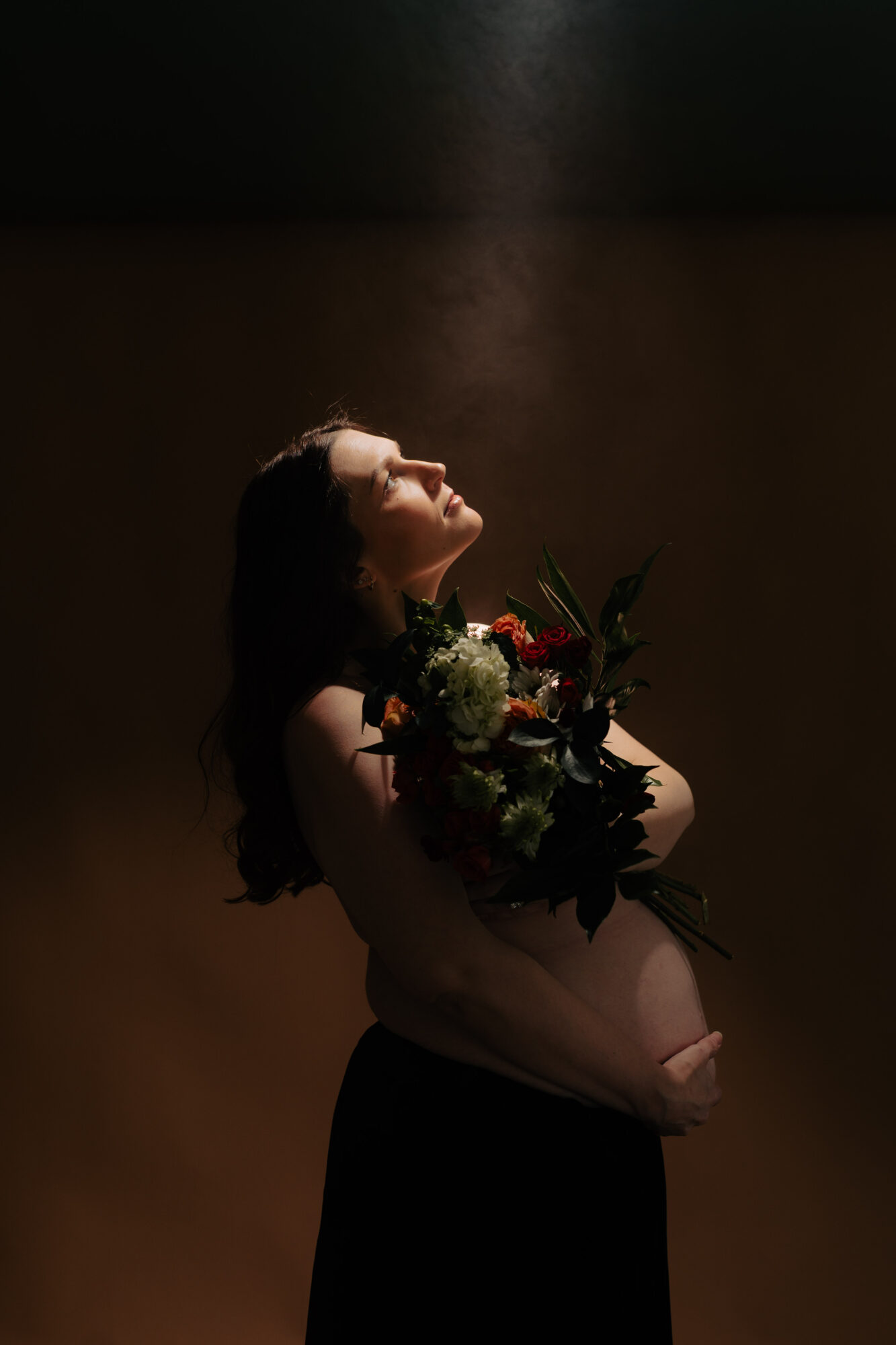 Woman holding a bouquet of flowers, with her head tilted back and eyes closed, against a dark background.