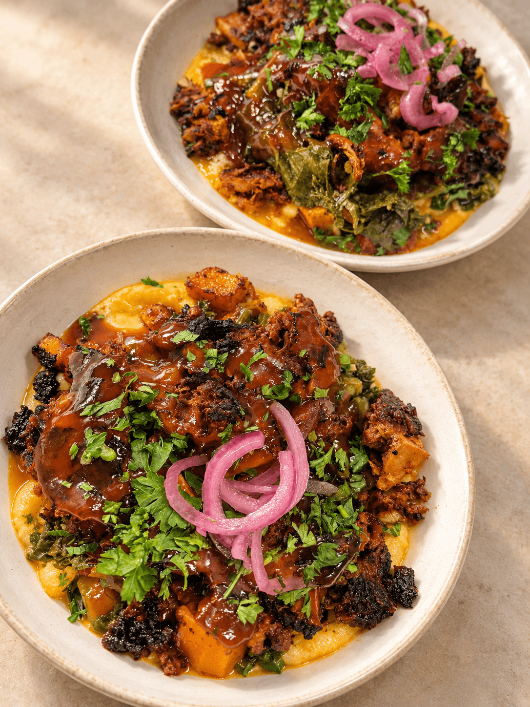 Two bowls of spicy, seasoned meat with herbs and pickled onions on top, served over a bed of vegetables.