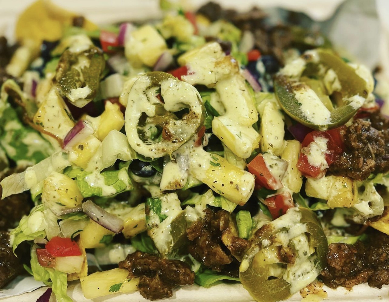 Close-up of a mixed salad with chopped vegetables and meat pieces, some green olives, and herbs, on a plate.