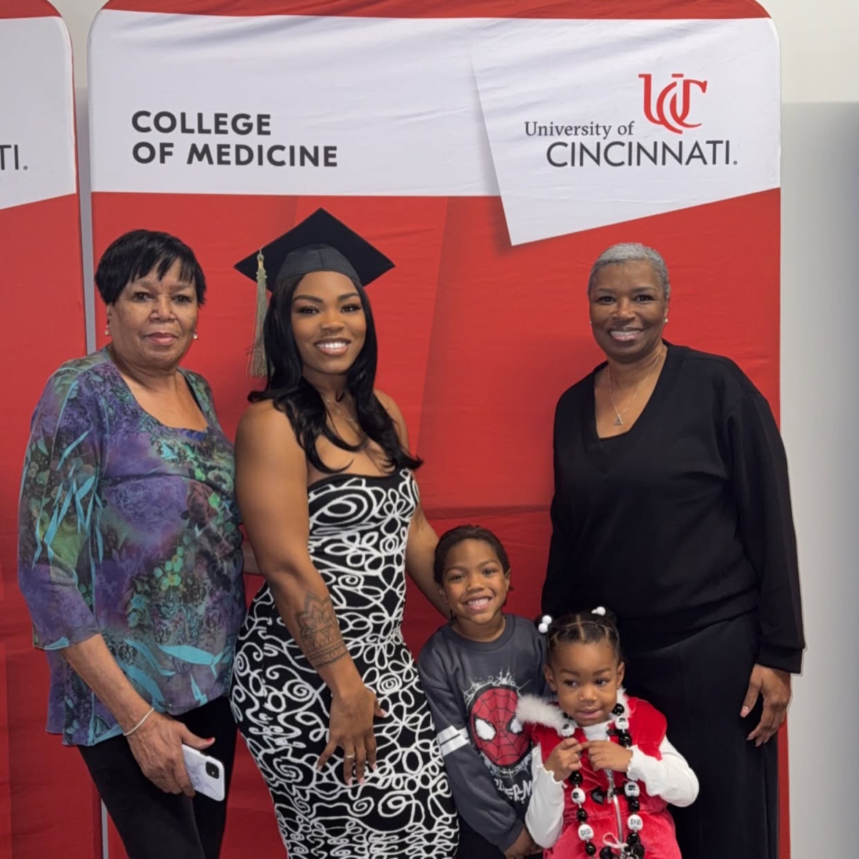 Four women and a girl standing in front of a red and white backdrop with university logos, smiling for the photo.