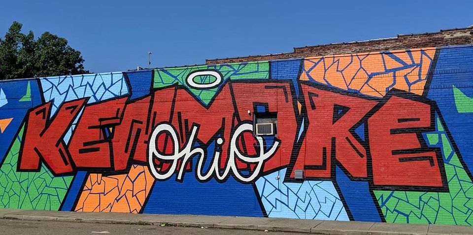 Colorful graffiti mural with large red lettering and geometric patterns on a wall beneath a blue sky.