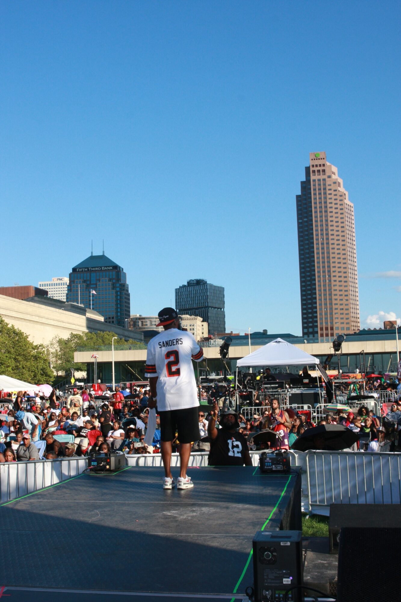 Runners gather at a city race start beneath tall buildings, with a person wearing a numbered shirt in the foreground.
