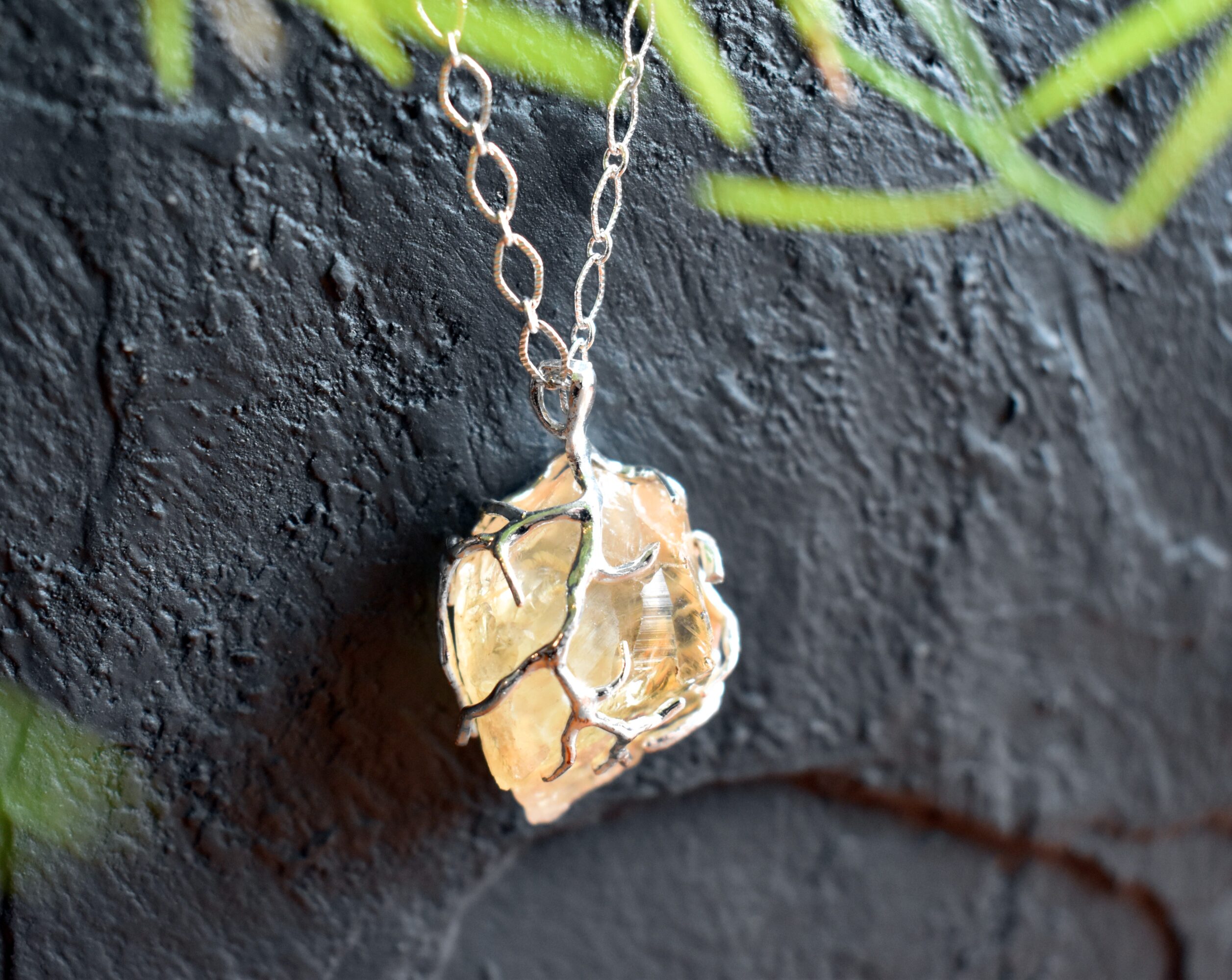 A silver chain with a translucent amber-colored pendant hangs against a dark textured wall.