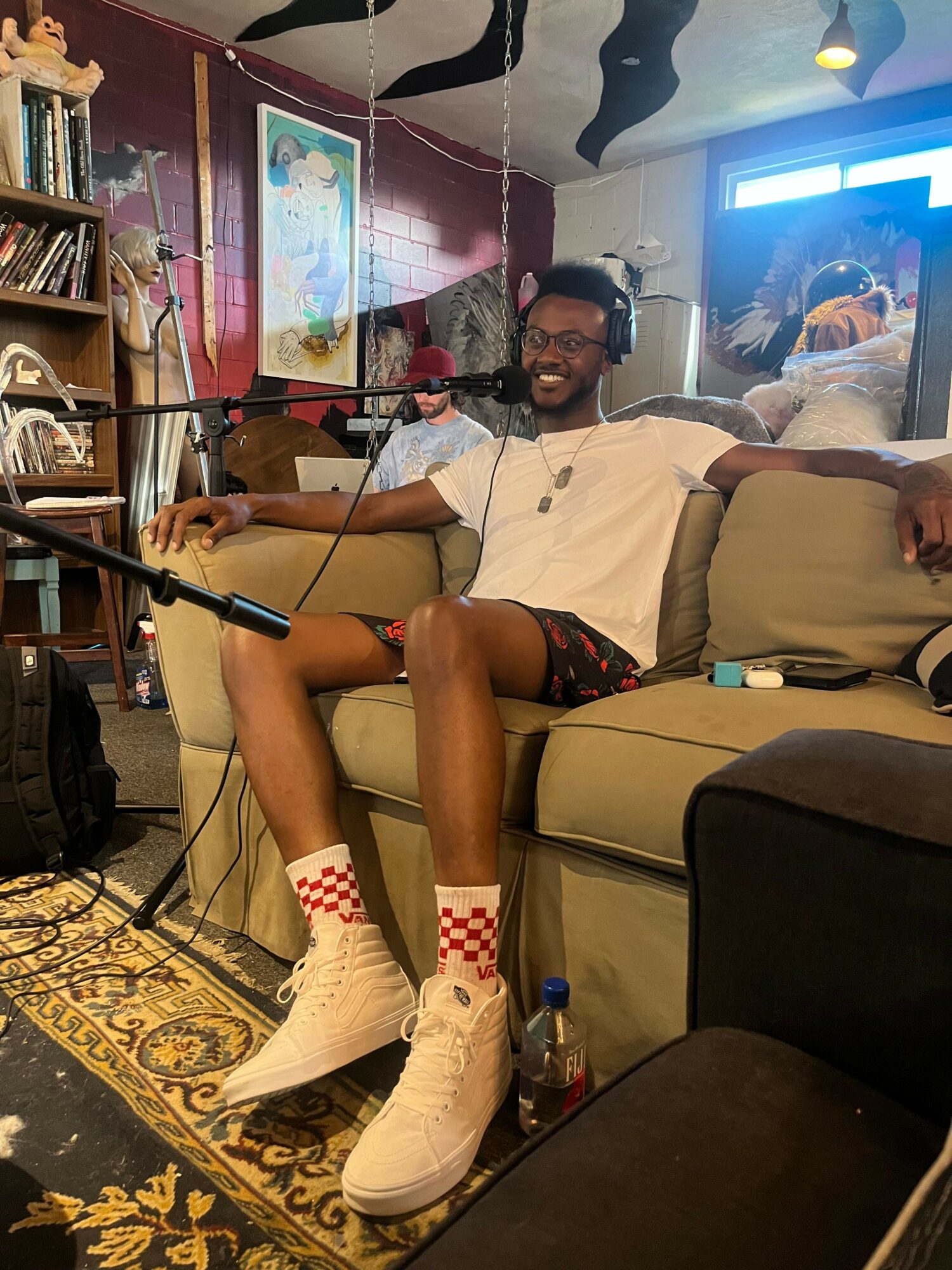Person sitting on a chair with legs crossed, wearing white sneakers and patterned socks, in a room with a patterned carpet and a TV.