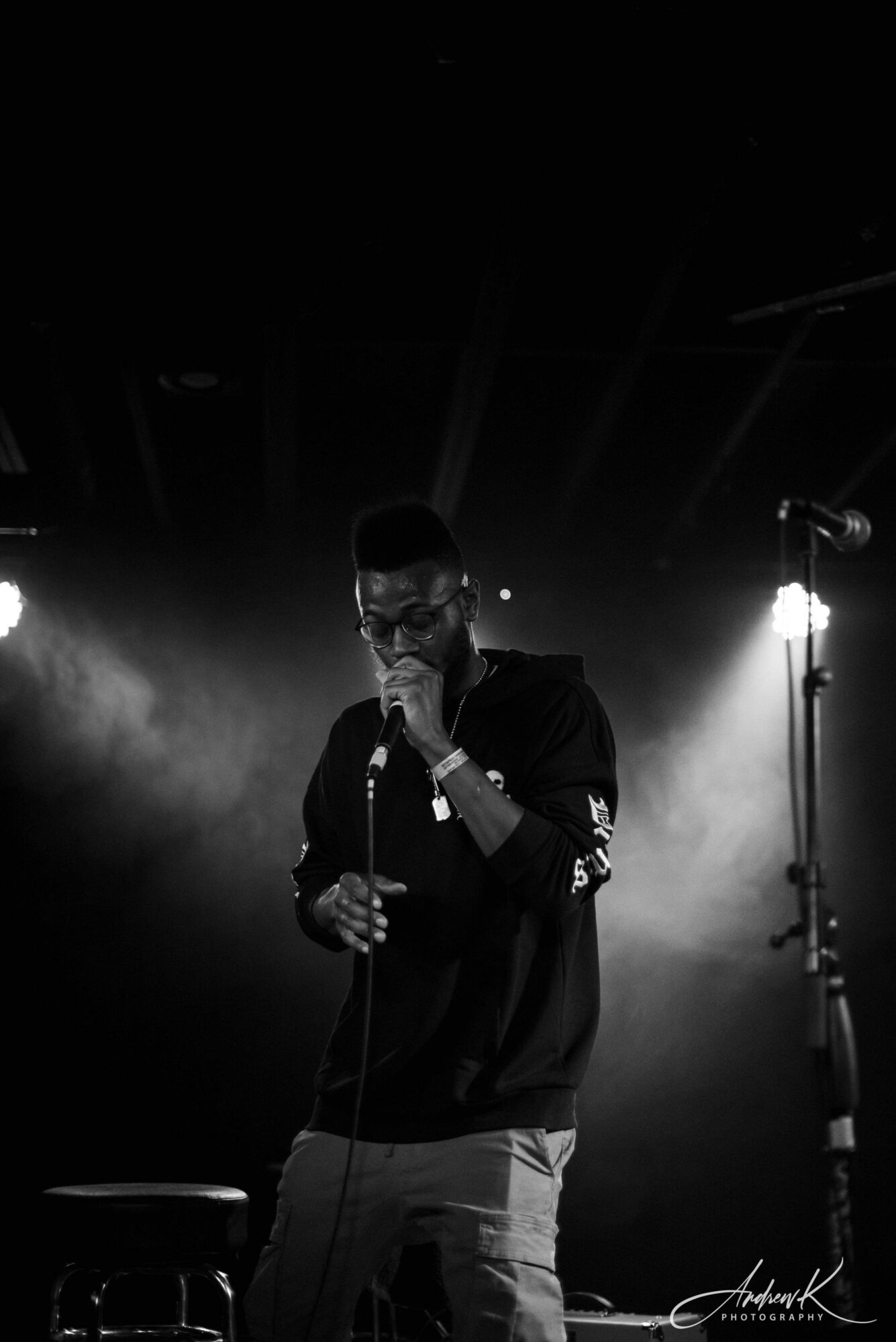Male singer holding microphone on stage with bright lights behind, performing in a dark setting.