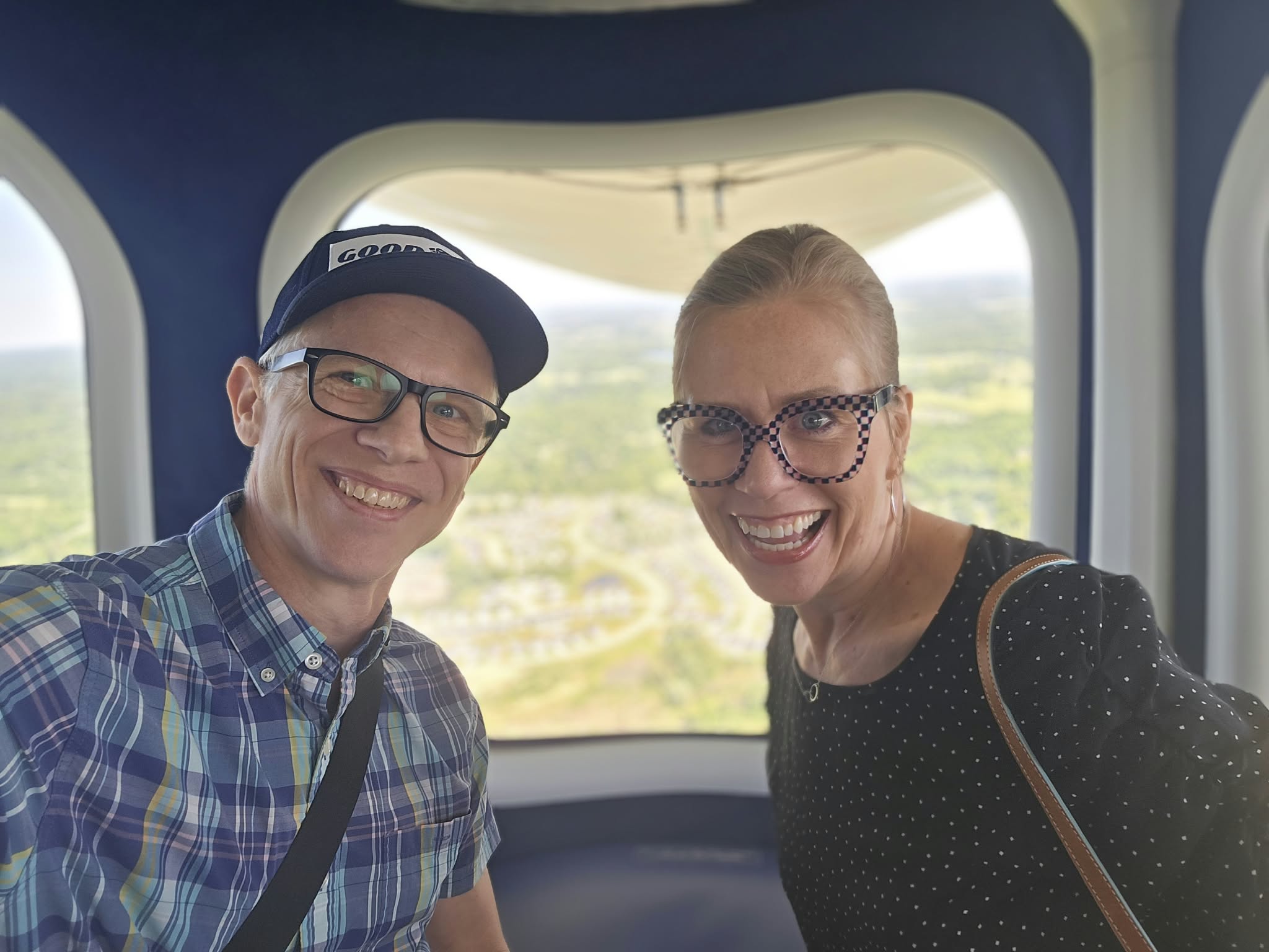 Two people smiling inside a vehicle with a scenic landscape outside the window.