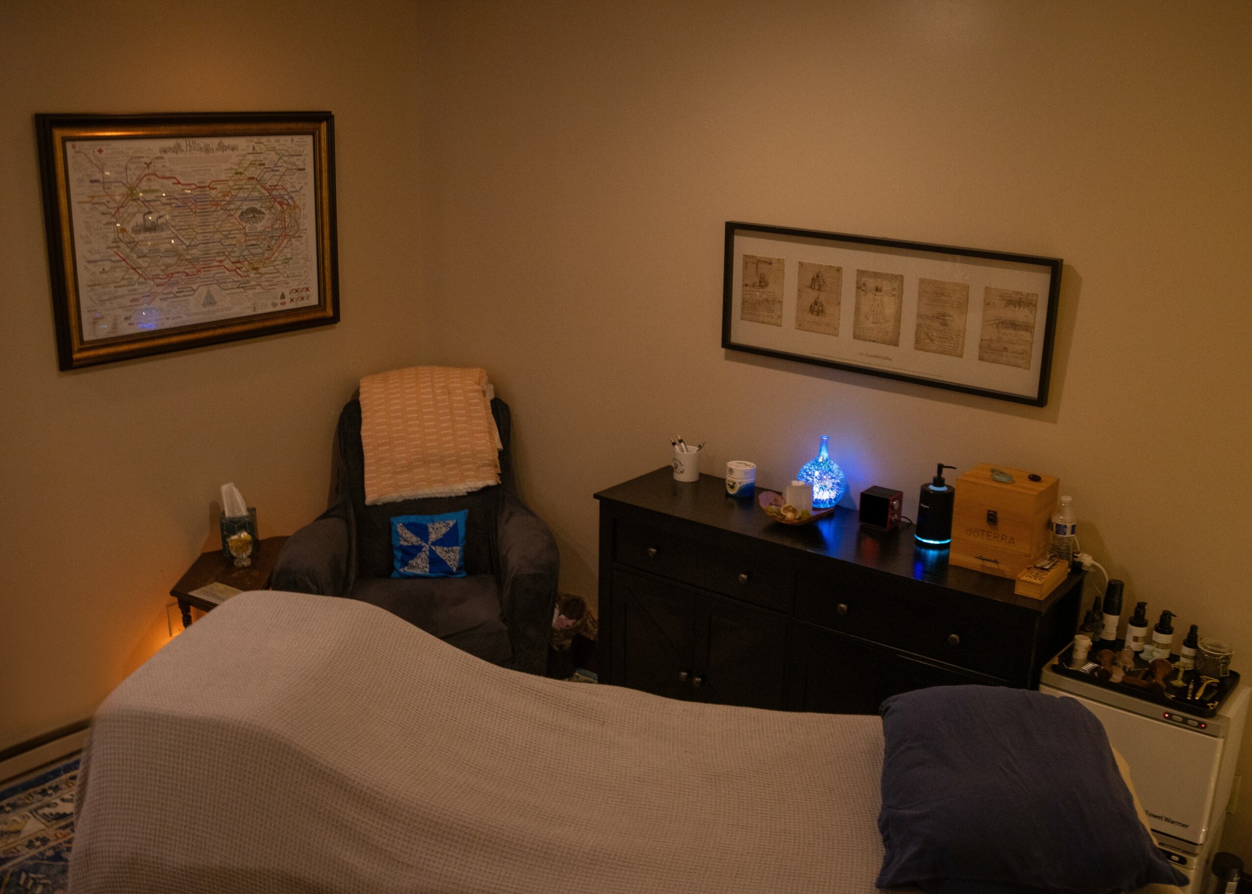Upright bedroom corner with bed, armchair, framed pictures, and a dresser with decorations.