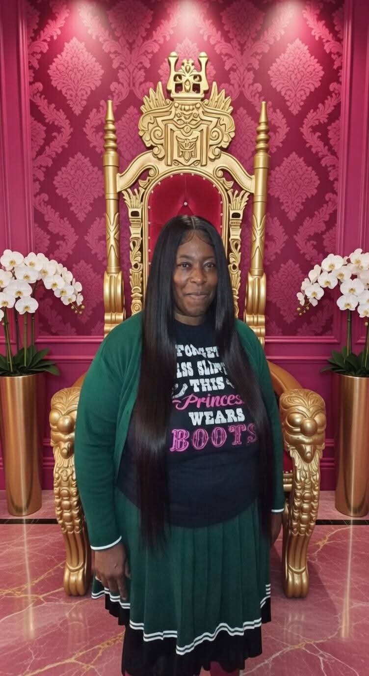 Woman with long black hair standing in front of a golden throne with pink background, flanked by white flowers.