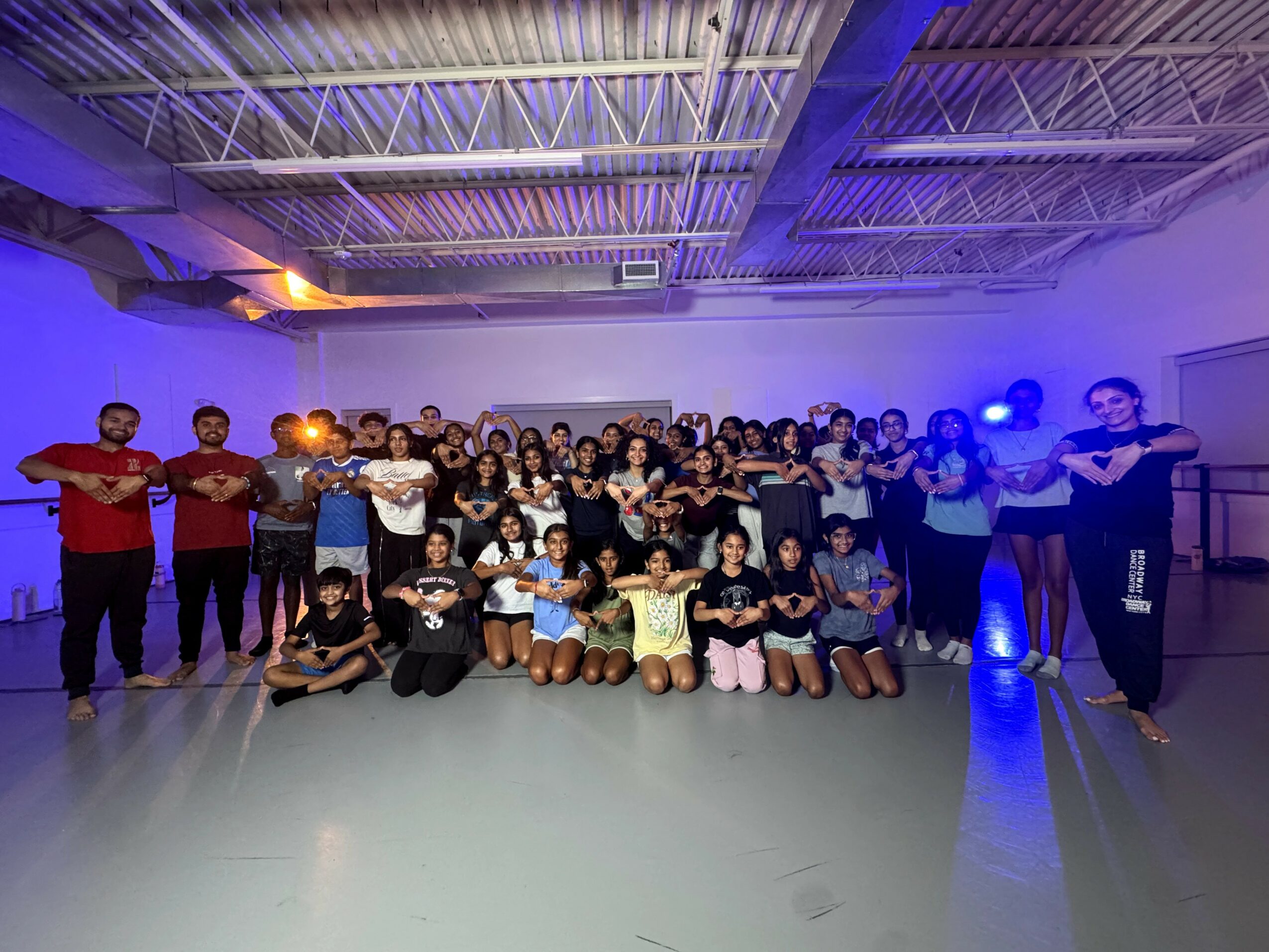 Group of people in a gymnasium with colorful lighting, some holding objects, posing for a photo.