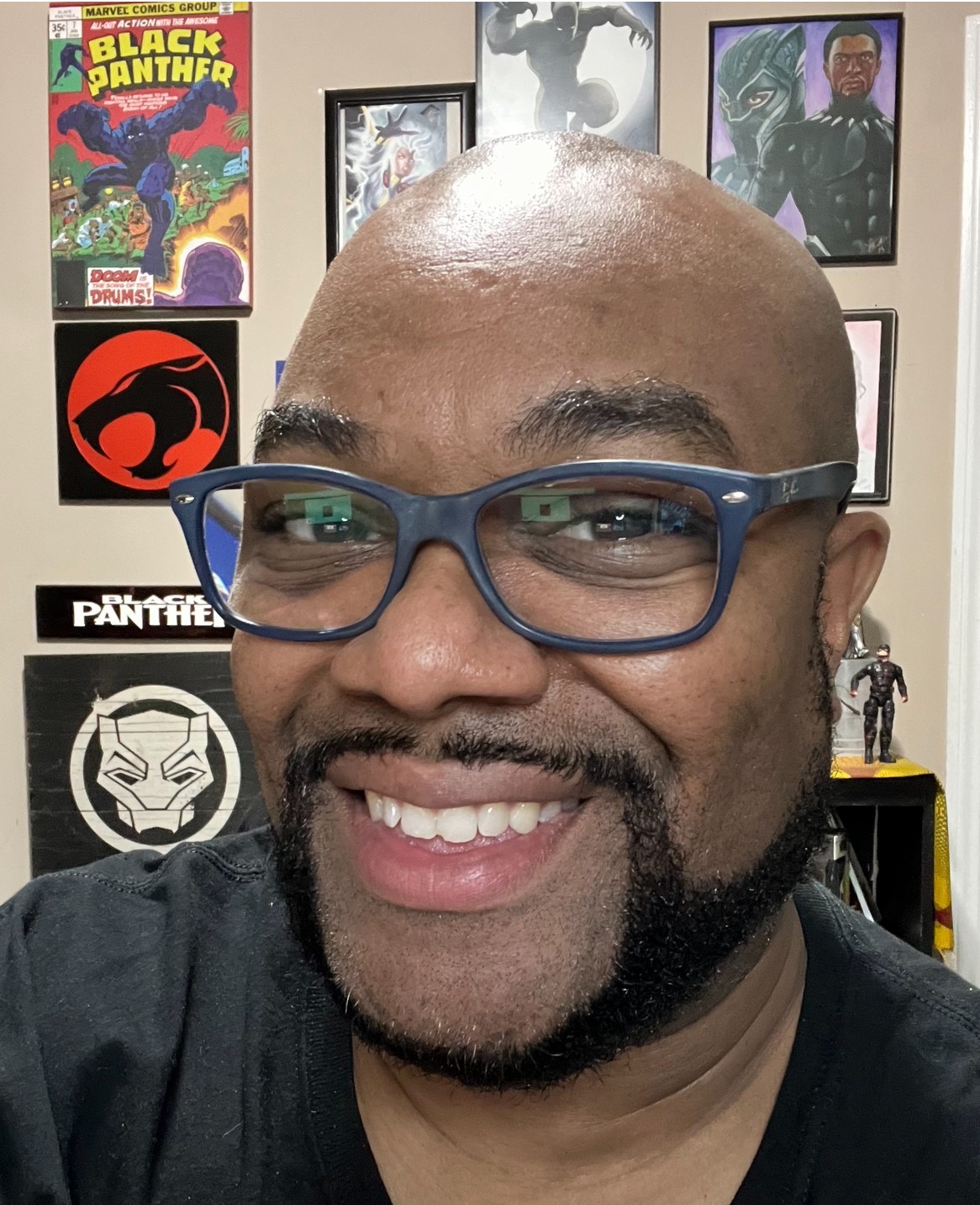 Smiling man with glasses in front of wall decorated with comic book and superhero posters.