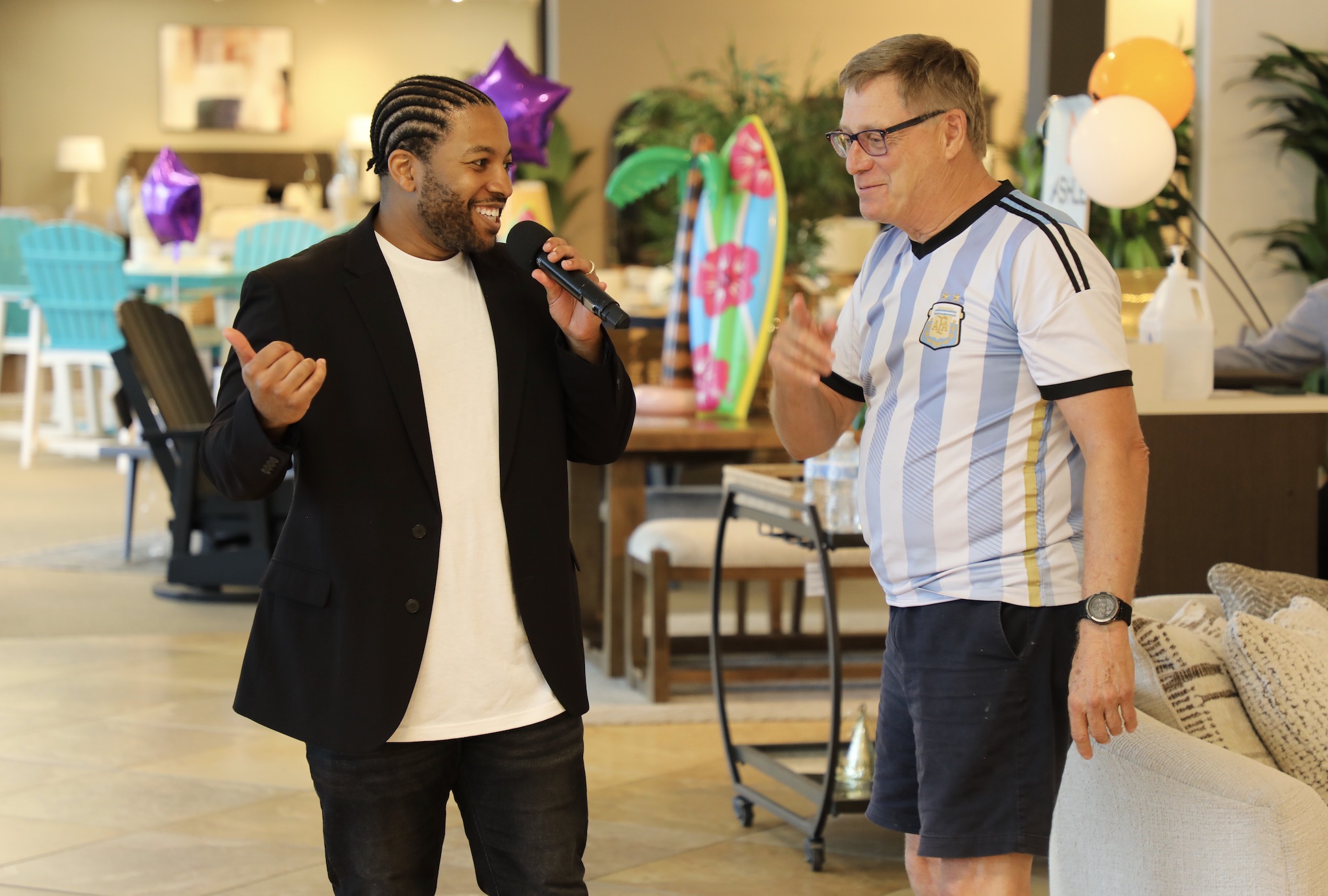 Two men talking and smiling at a party with balloons and decorations in the background.