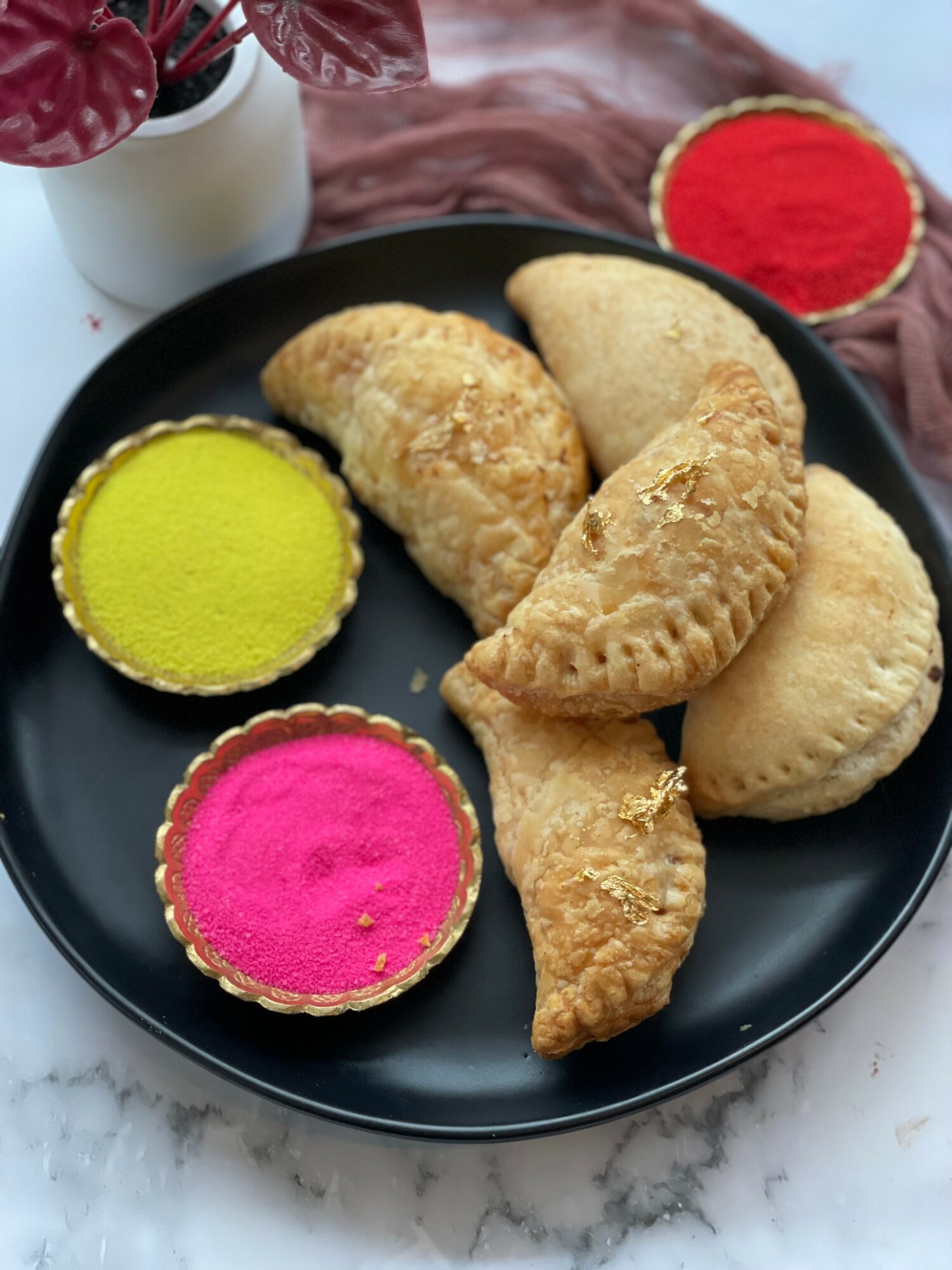 Plate with three fried snacks and two colorful dipping bowls, one yellow and one pink, on a black plate.