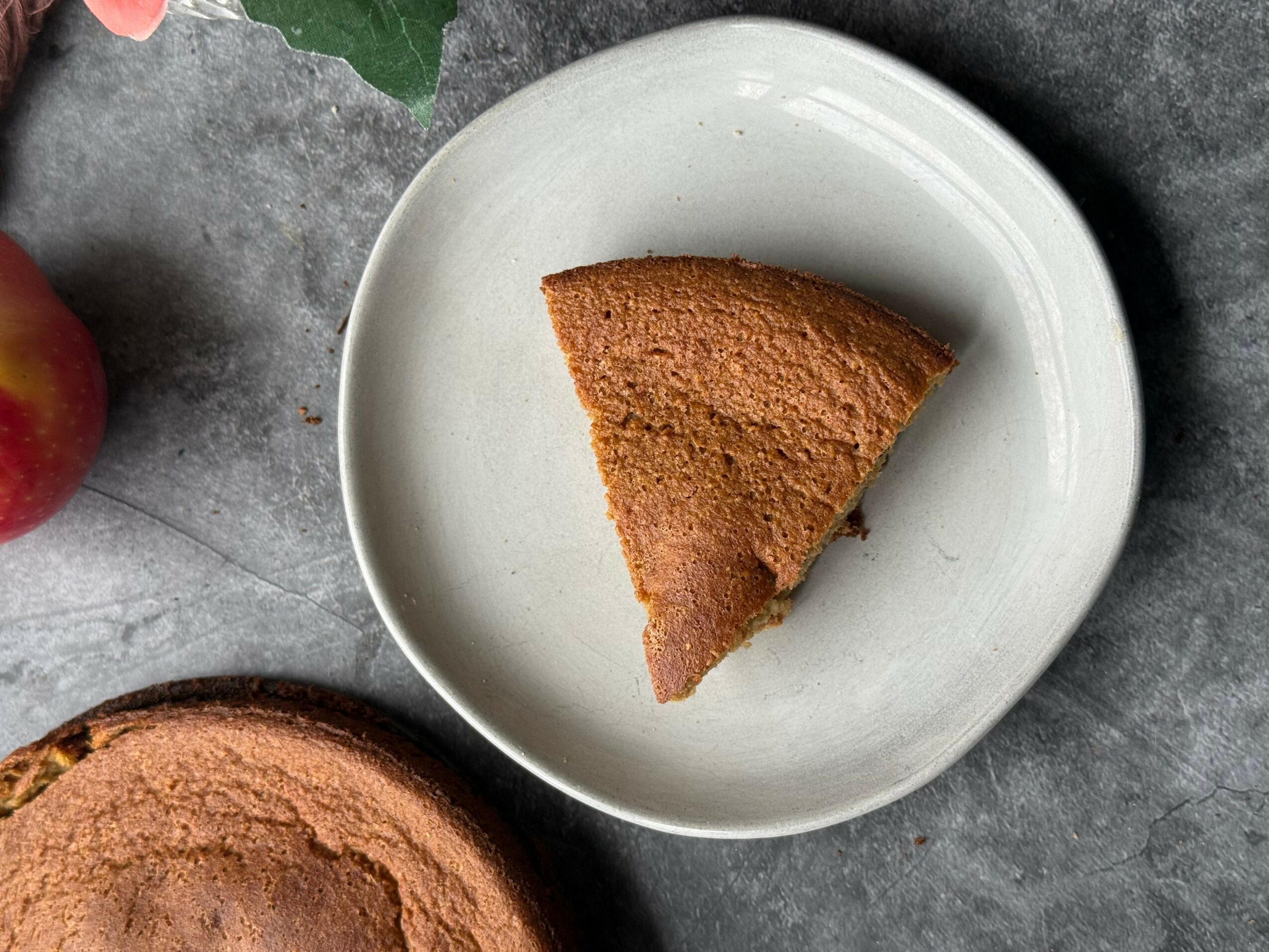 A slice of cake on a white plate, with a gray textured surface background.