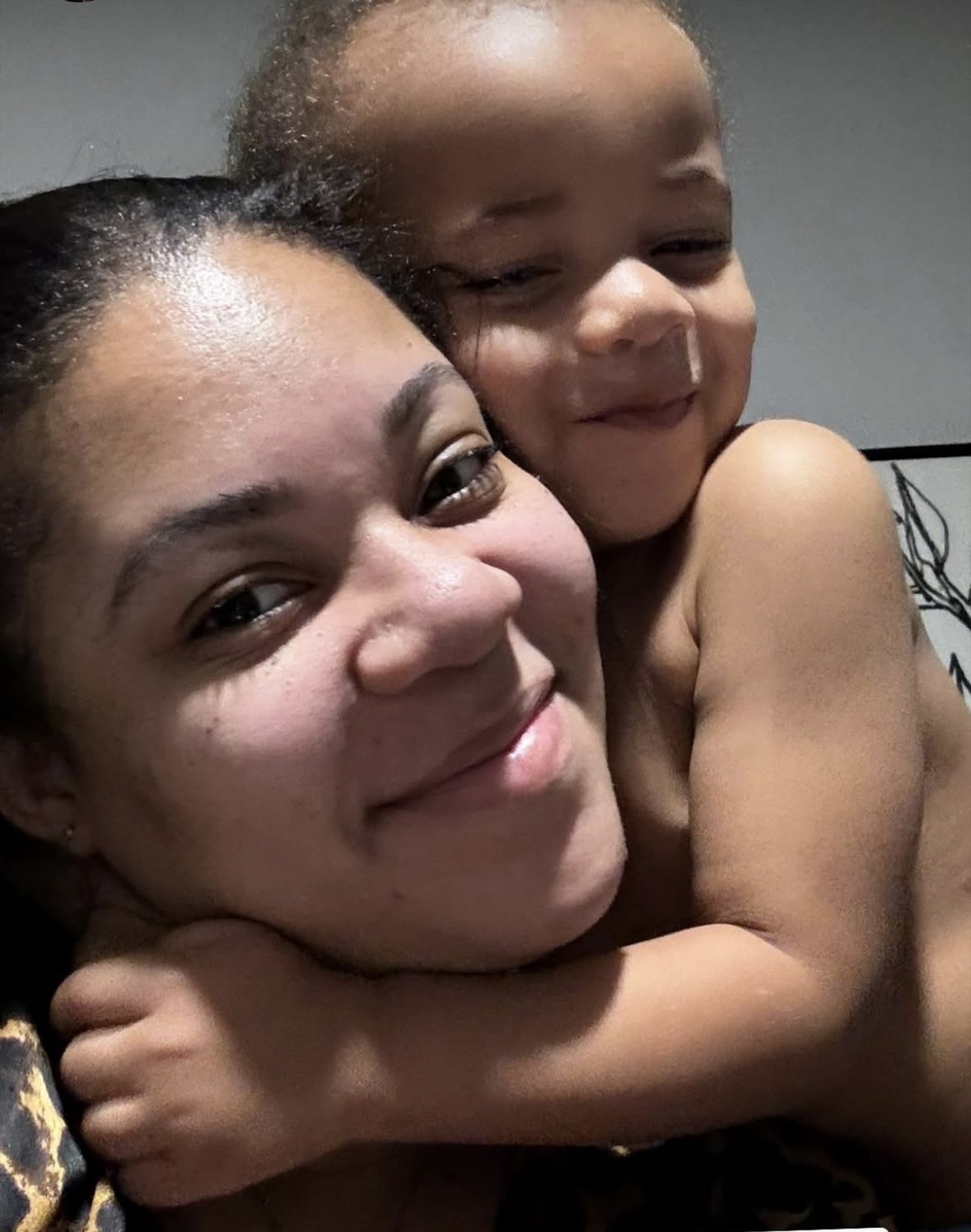 A woman and a young child hugging and smiling, close-up shot, indoors.