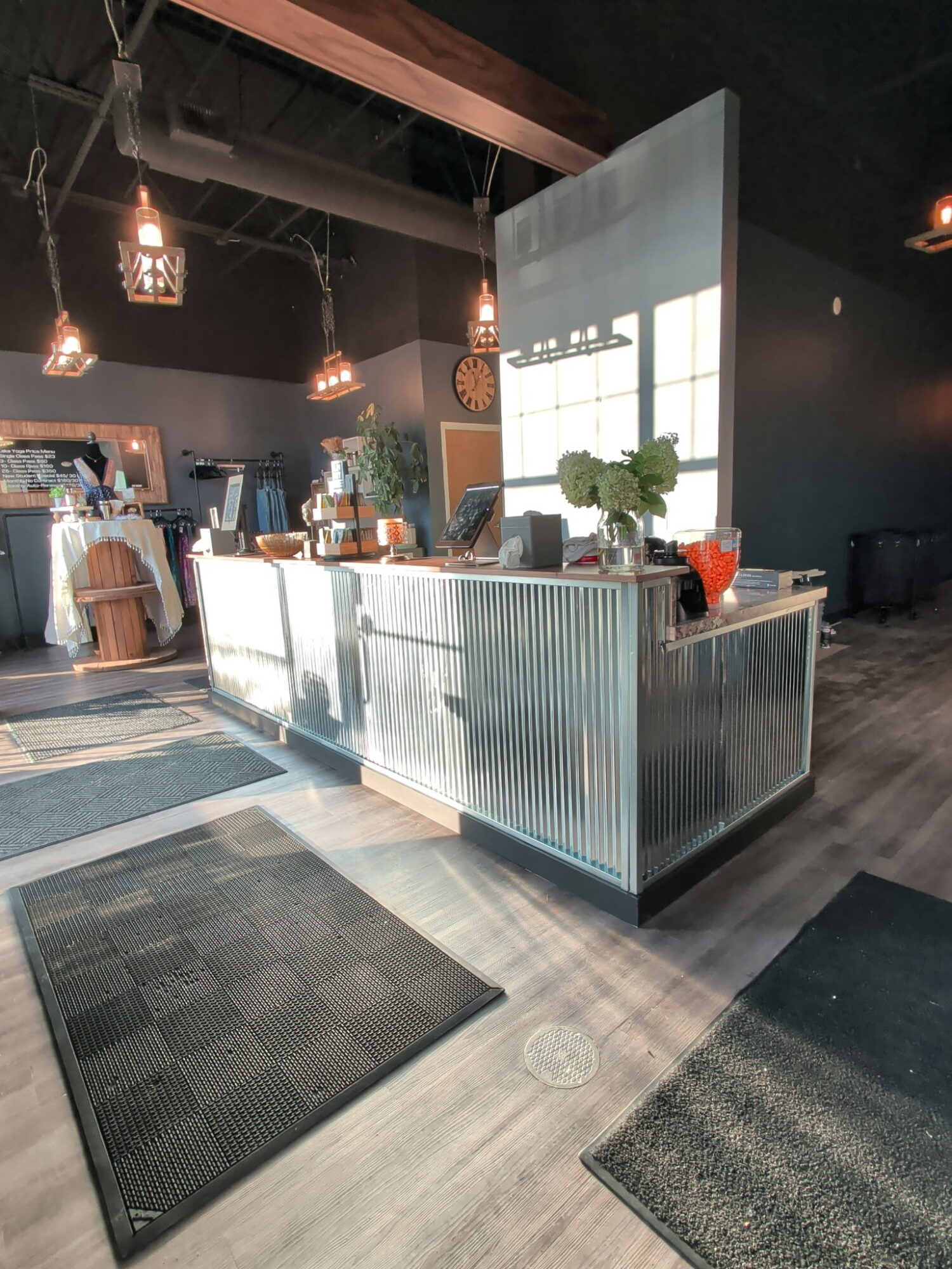 Modern reception desk with plants and decor in a stylish interior space, with hanging lights and a large window.