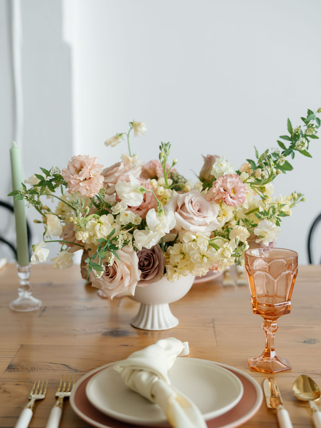Flower arrangement with pink and white flowers in a white vase on a wooden table, with a pink glass and tableware.