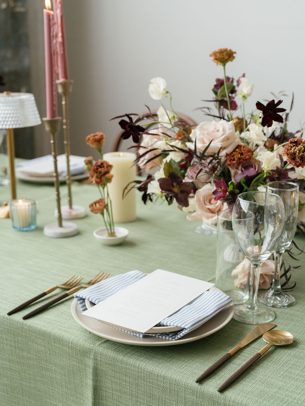 Table setting with a plate, napkin, cutlery, and a floral centerpiece, on a green tablecloth.