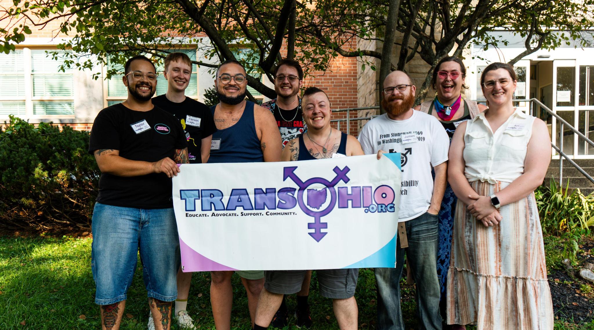 A group of people stand outdoors holding a banner reading “Trans Ohio 2023.”