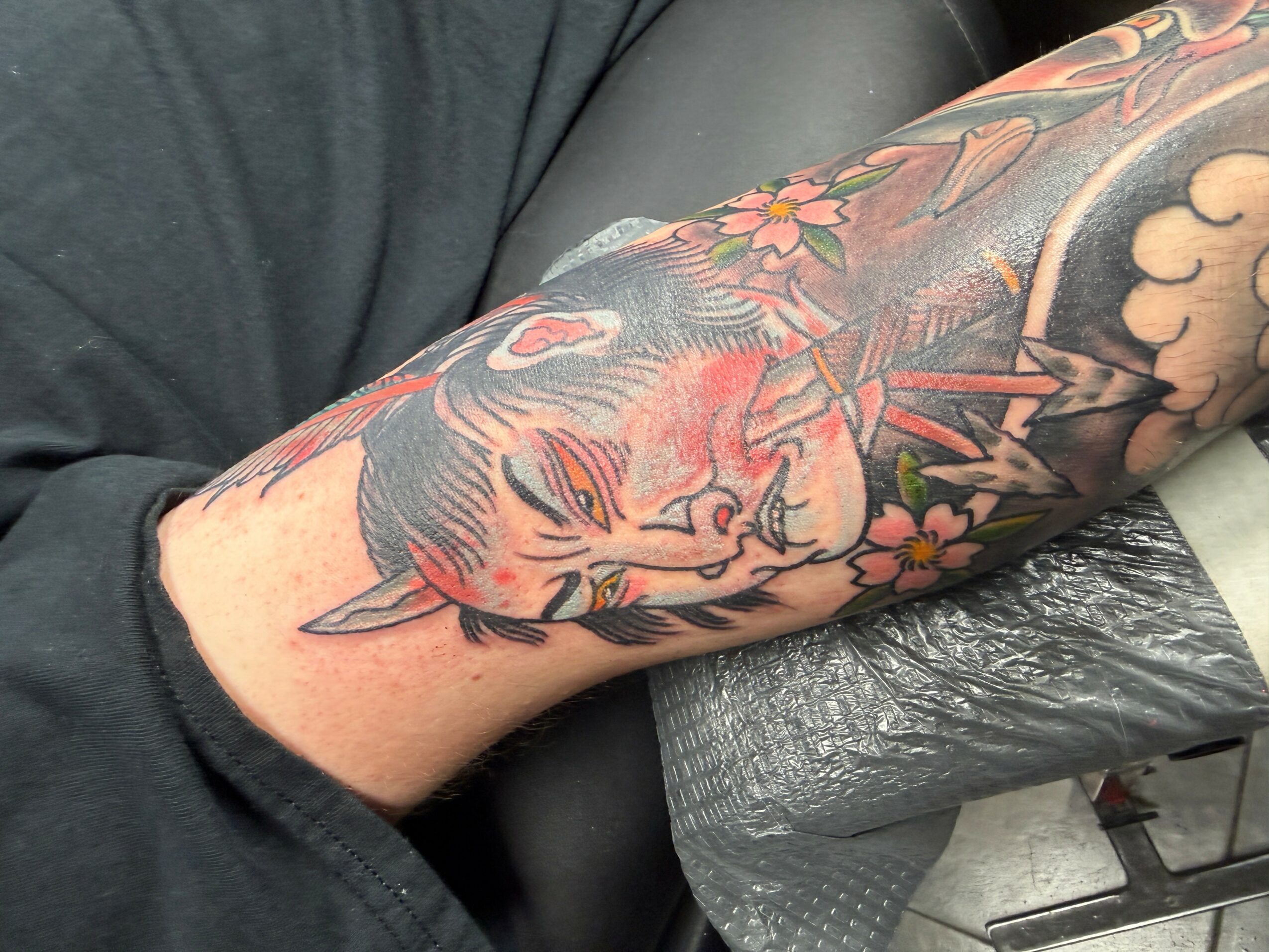 Colorful tattoo of a tiger's face with flowers on a person's arm, with visible skin and clothing.