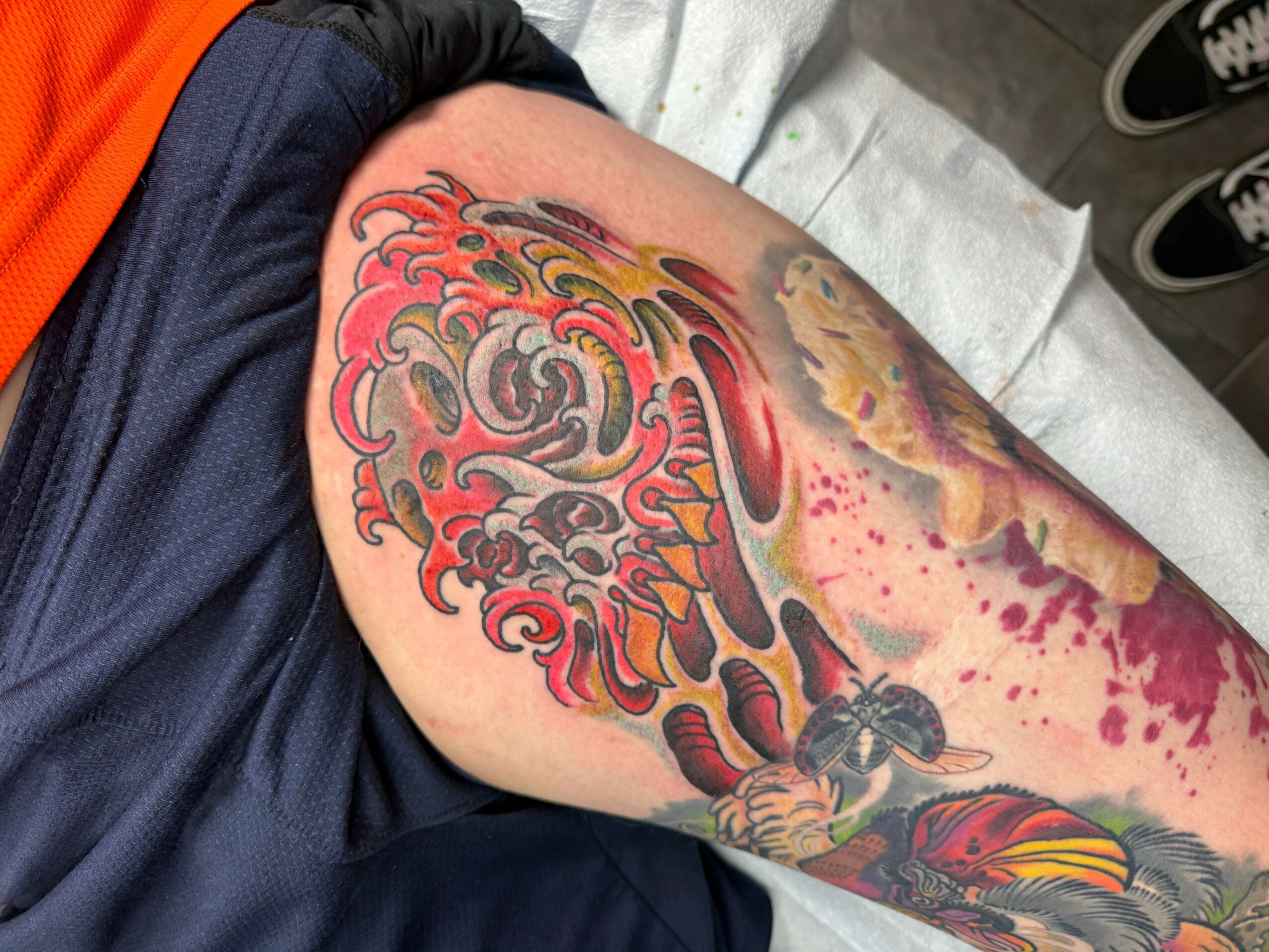 Colorful tattoo on person's upper arm featuring a lion's face with a mane, flames, and a spider hanging from the mane.