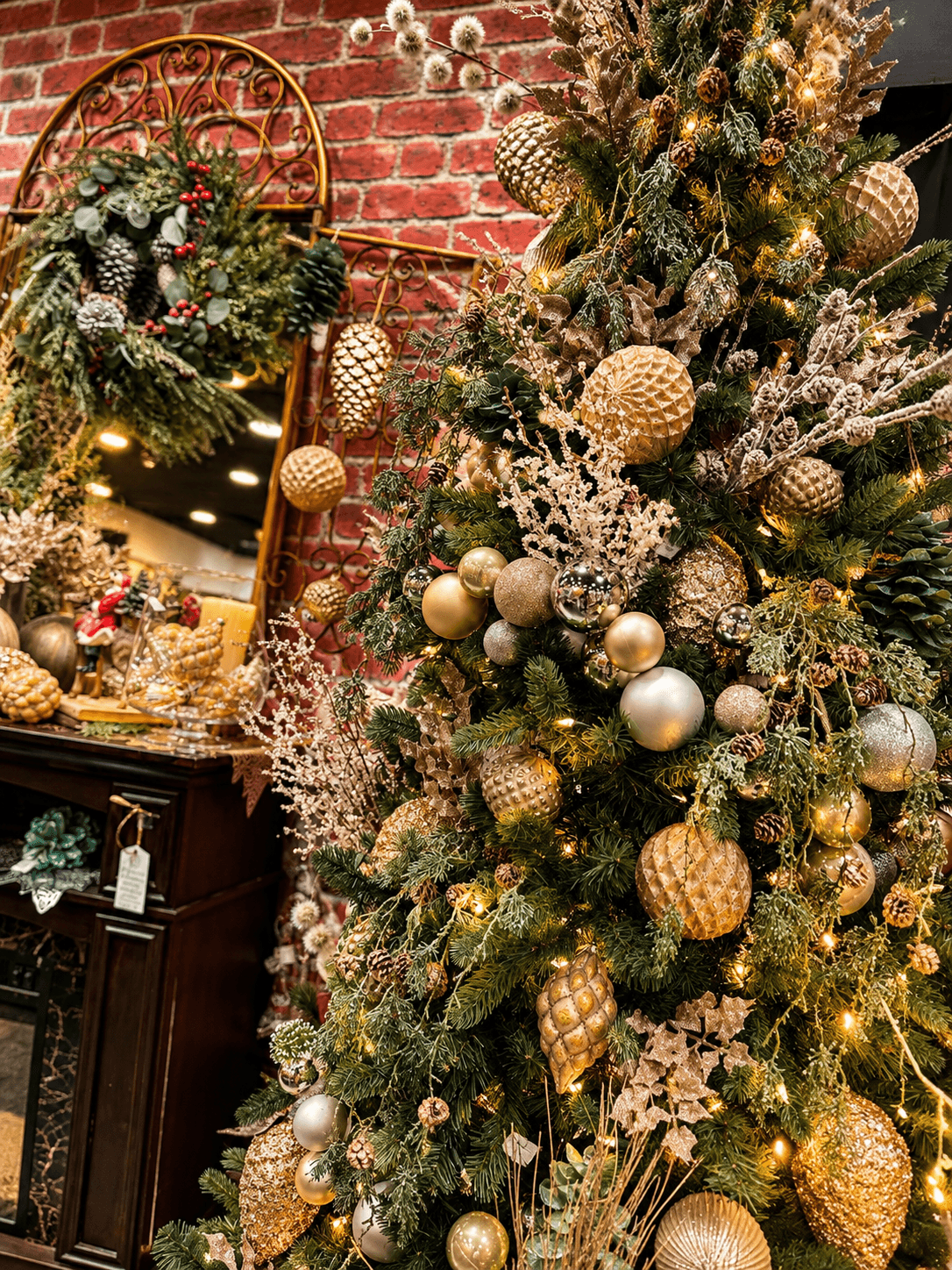 Decorated Christmas tree with gold ornaments beside a brick wall and wooden cabinet.
