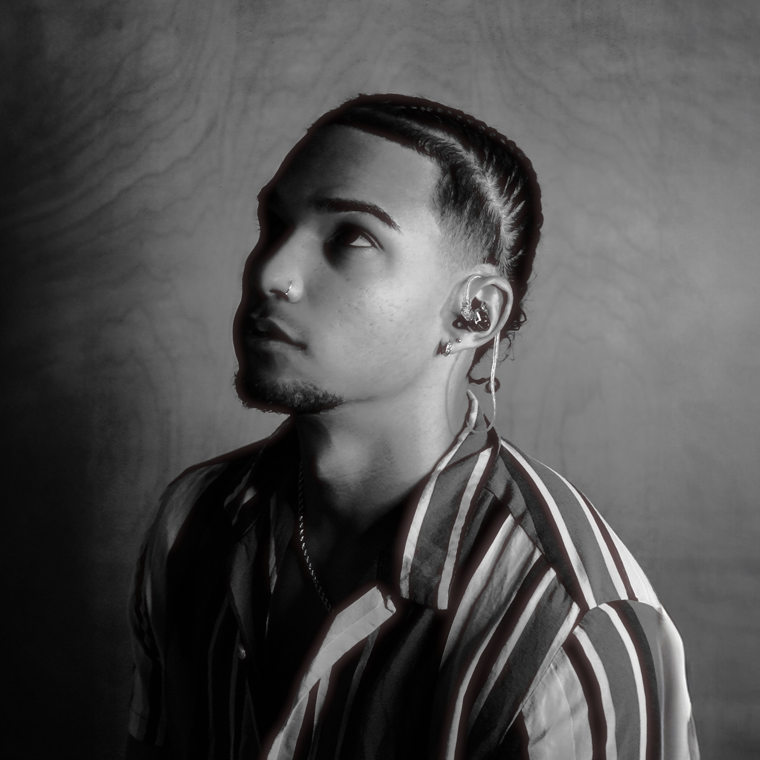 Black-and-white portrait of a person with short hair and an earring, wearing a striped shirt and looking upward.