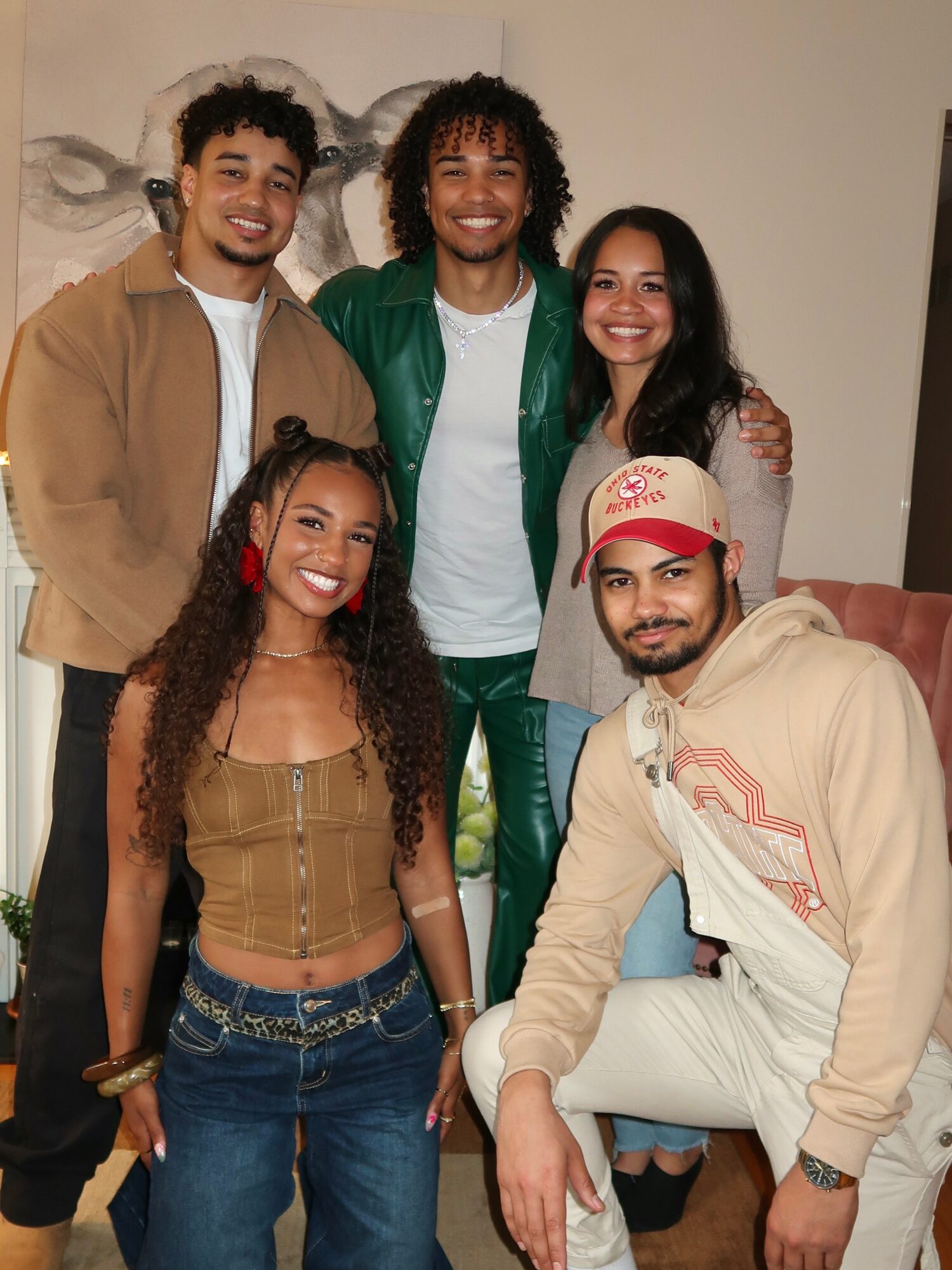 Five people pose together indoors in front of a wall decoration.
