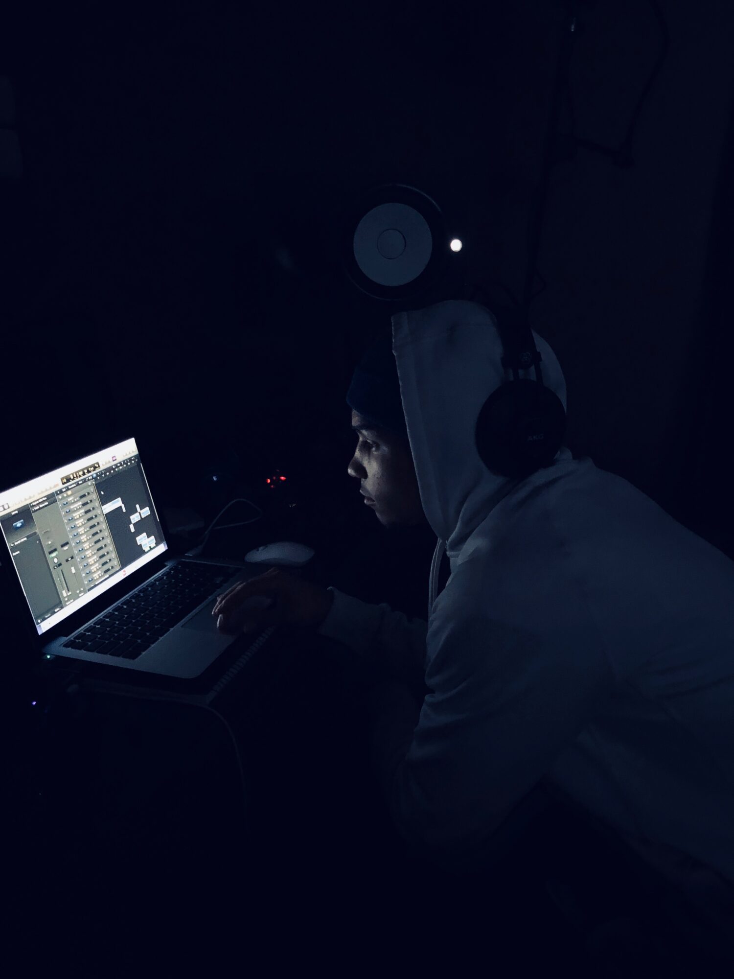 A person wearing headphones sits at a laptop in a dark room, with a speaker mounted above.