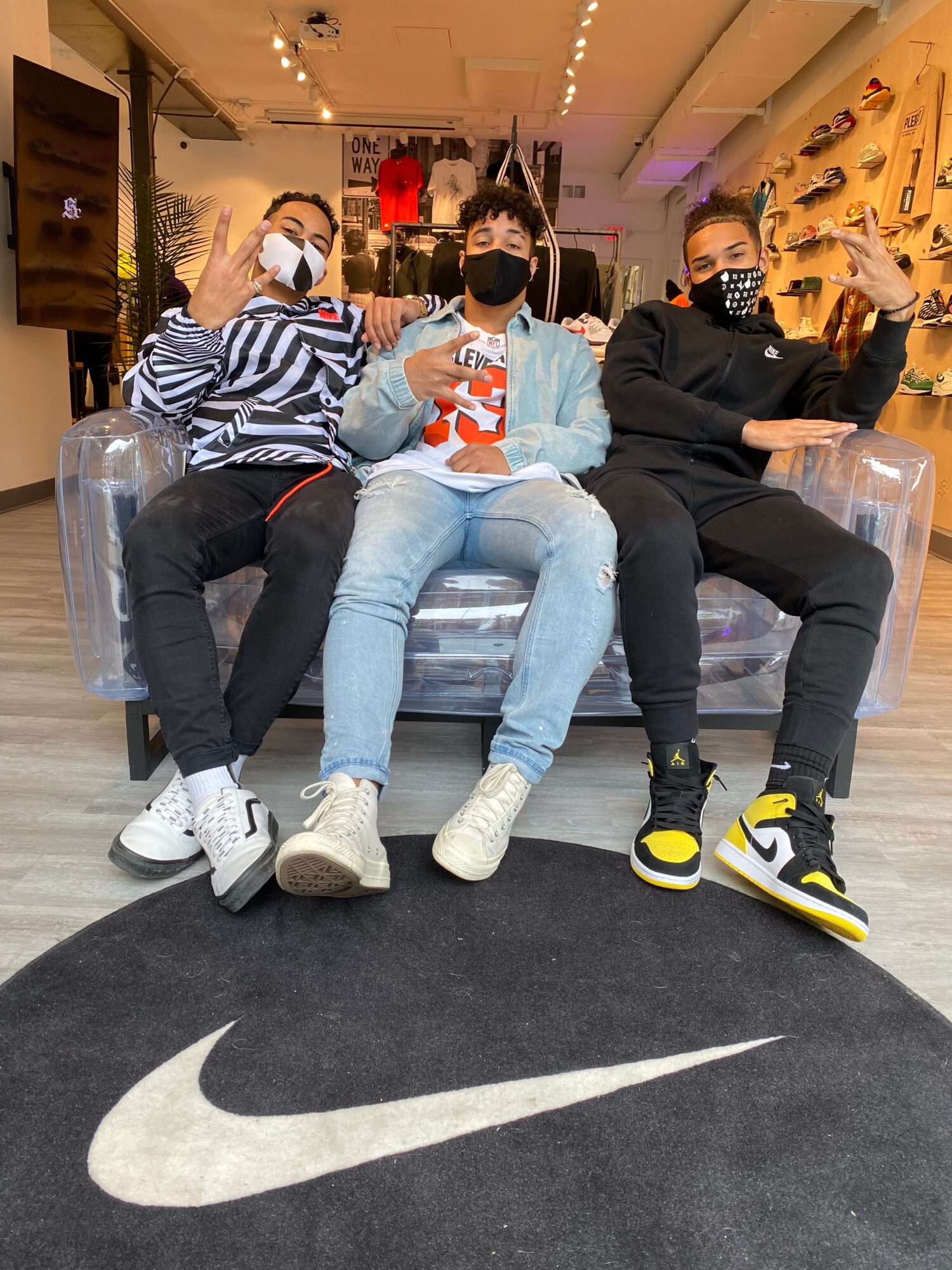 Four people sit on chairs beside a large white swoosh on a black floor.