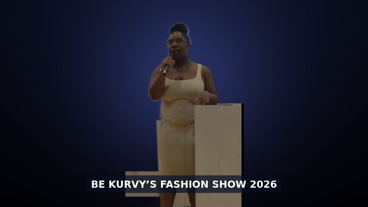 Woman standing behind a podium speaking at an event with a dark background, caption reads 'BE KURVY'S FASHION SHOW 2026'.