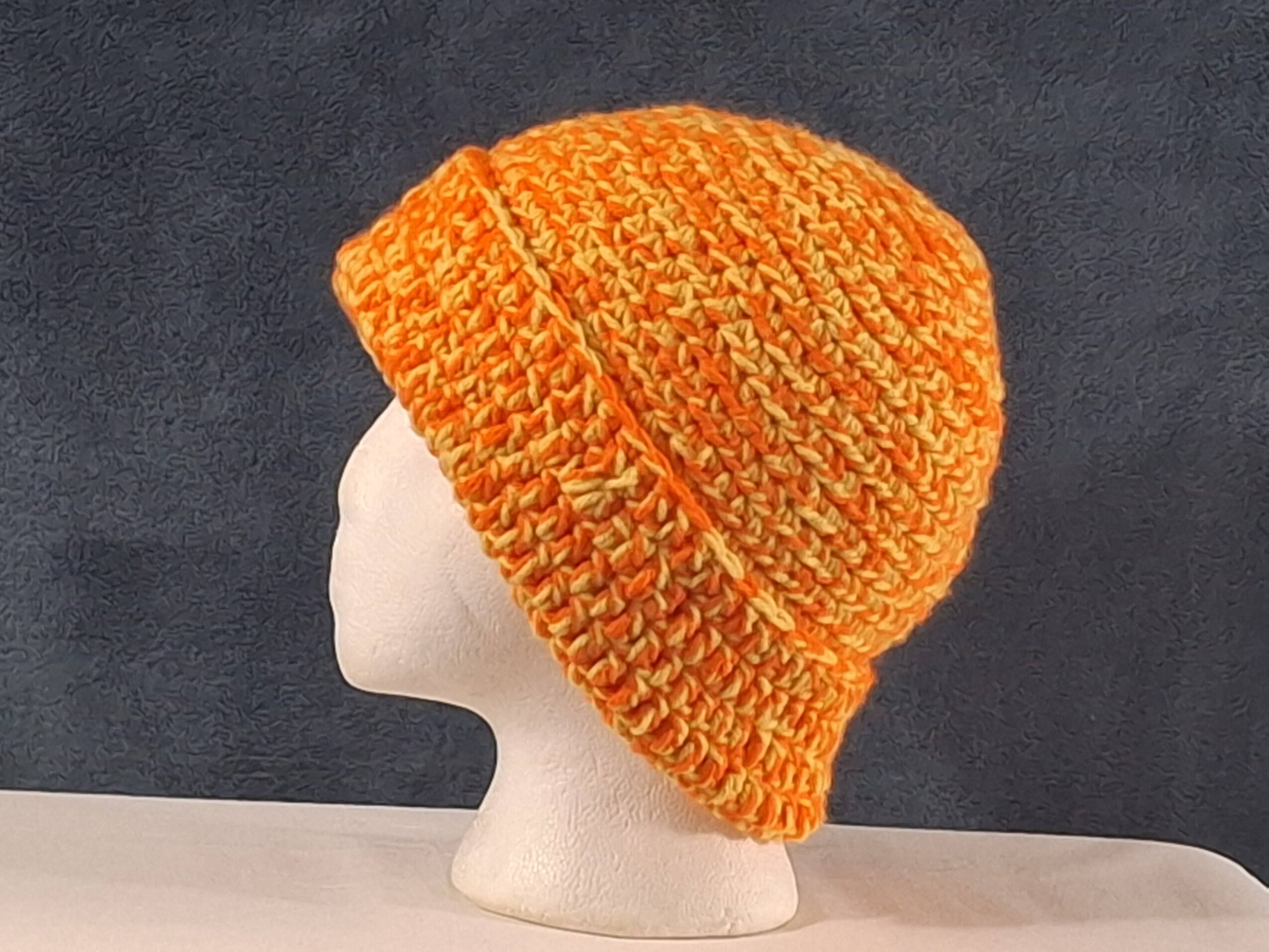 Orange knitted beanie displayed on a white mannequin head against a dark background.