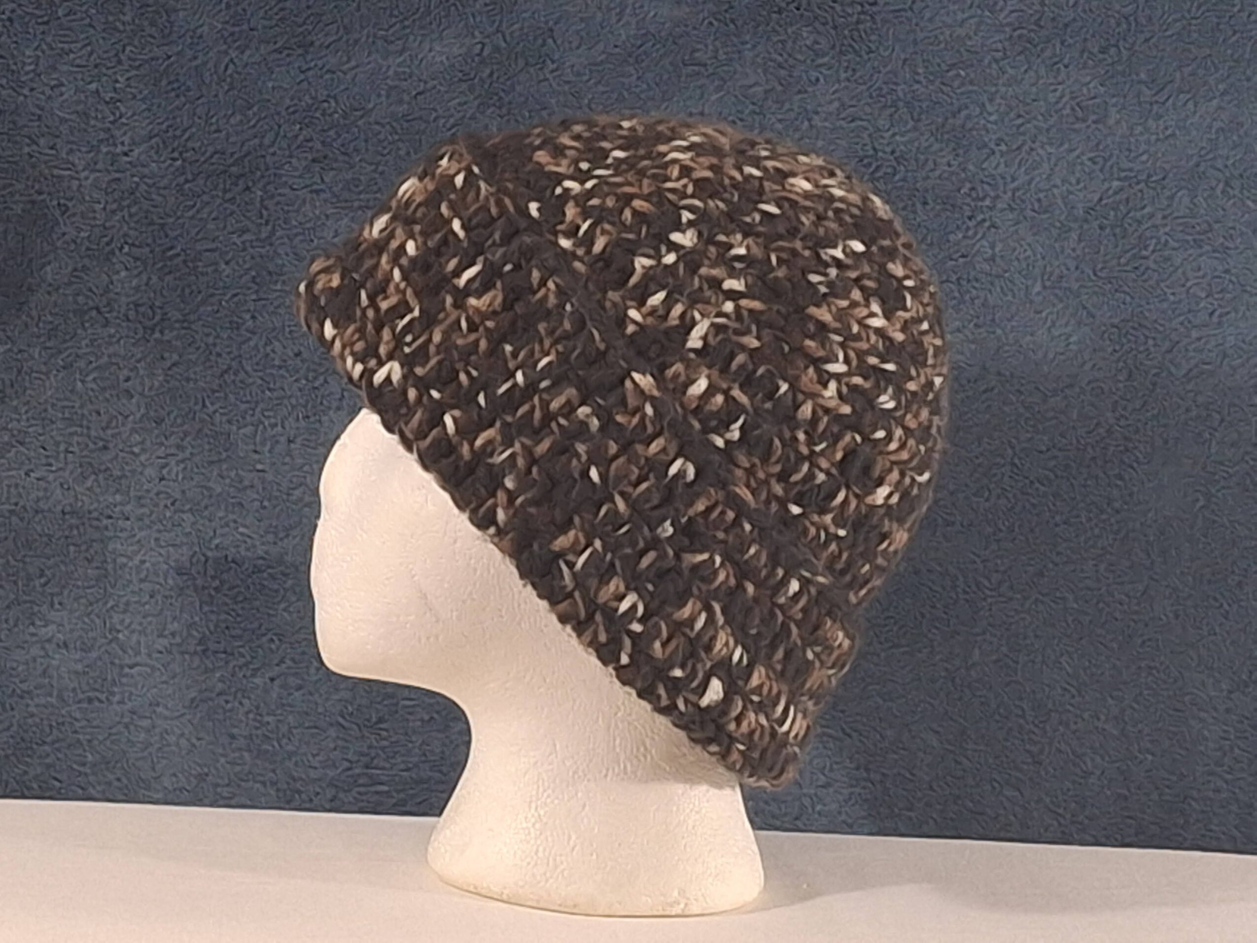 A brown knitted hat on a white mannequin head against a gray background.