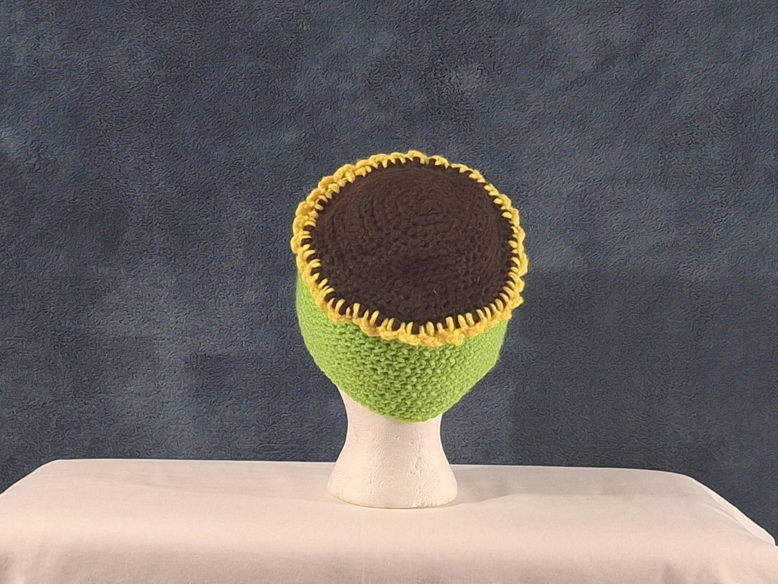 A green and yellow flower-shaped object with a dark brown center stands on a white base against a gray background.
